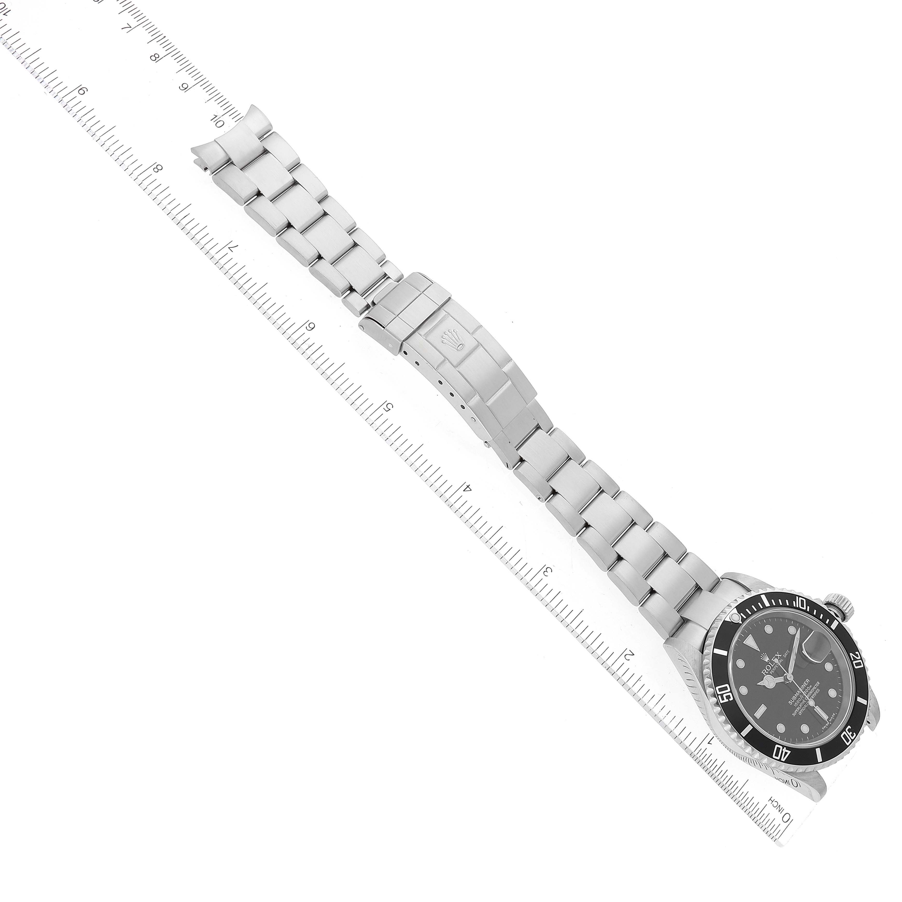 The image shows an aerial view of a Rolex Submariner 16610 Men
s Stainless Steel Black Dial 16610 Men
s Stainless Steel Black Dial watch, displaying its bracelet, clasp, and face next to a ruler for size reference.