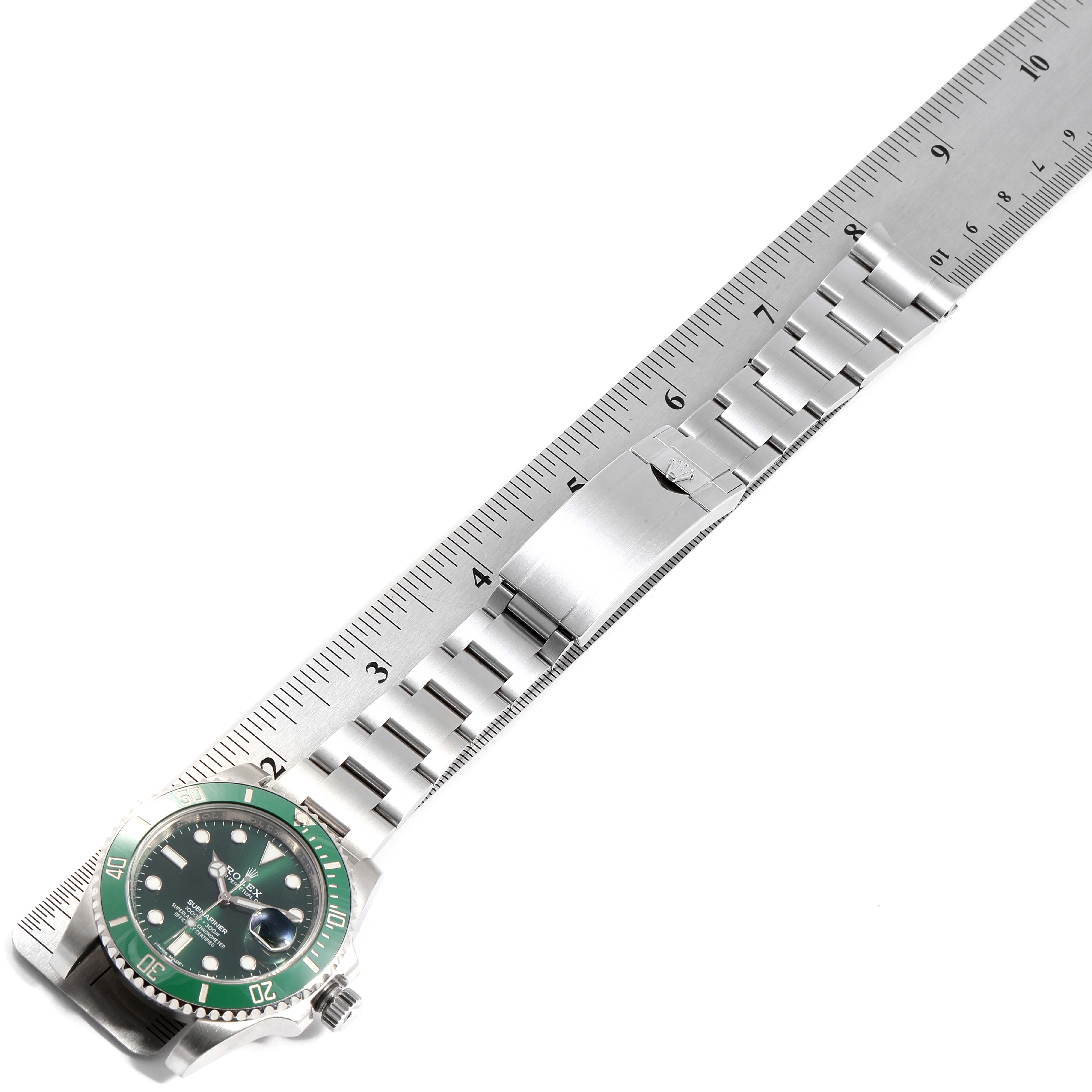 The image shows a top view of a Rolex Submariner 116610LV Men
s Stainless Steel Green Dial 116610LV Men
s Stainless Steel Green Dial watch with a green bezel and dial, alongside a metal ruler for measurement.