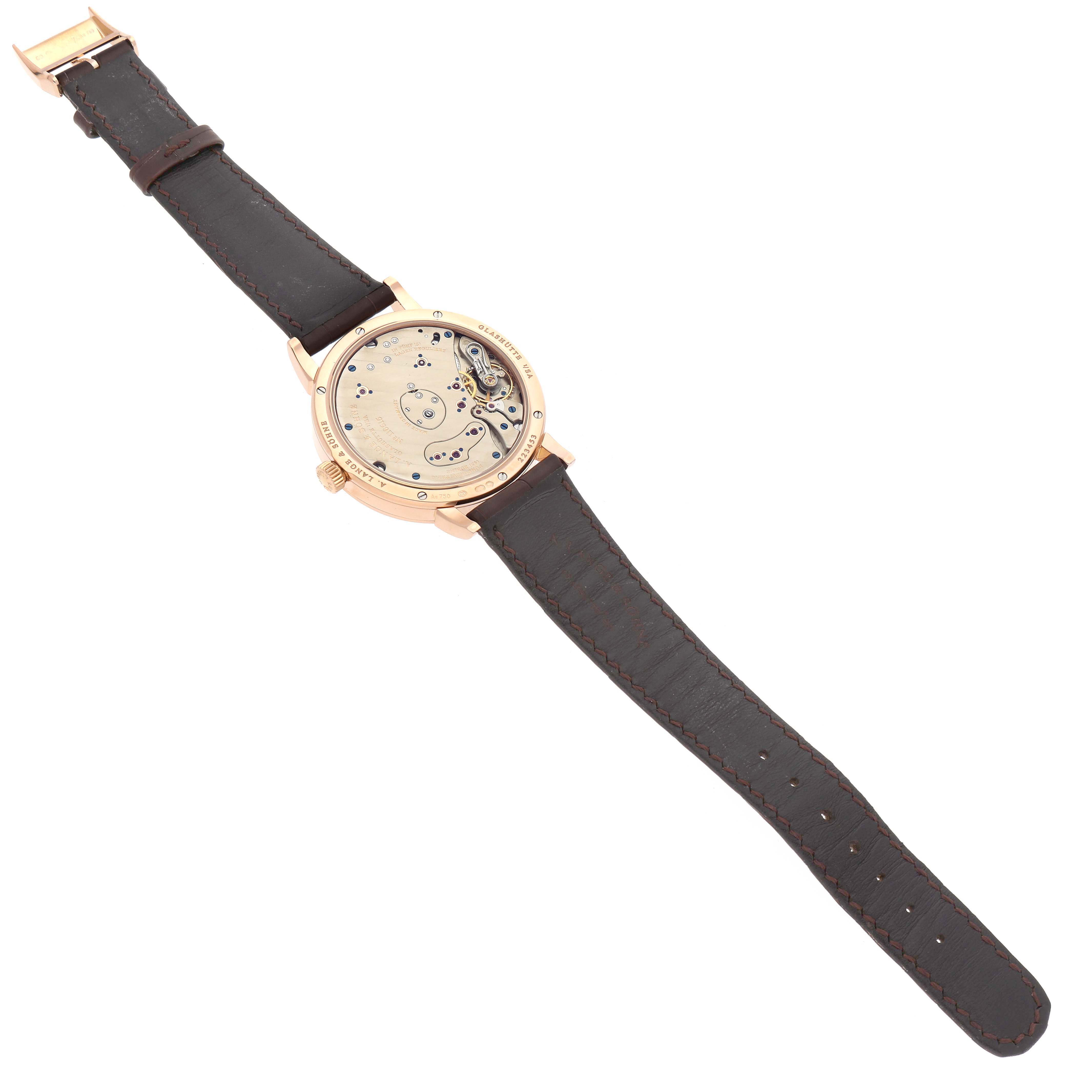 The image shows a Lange 1 watch by A. Lange & Söhne from the back, revealing its intricate movement and brown leather strap.