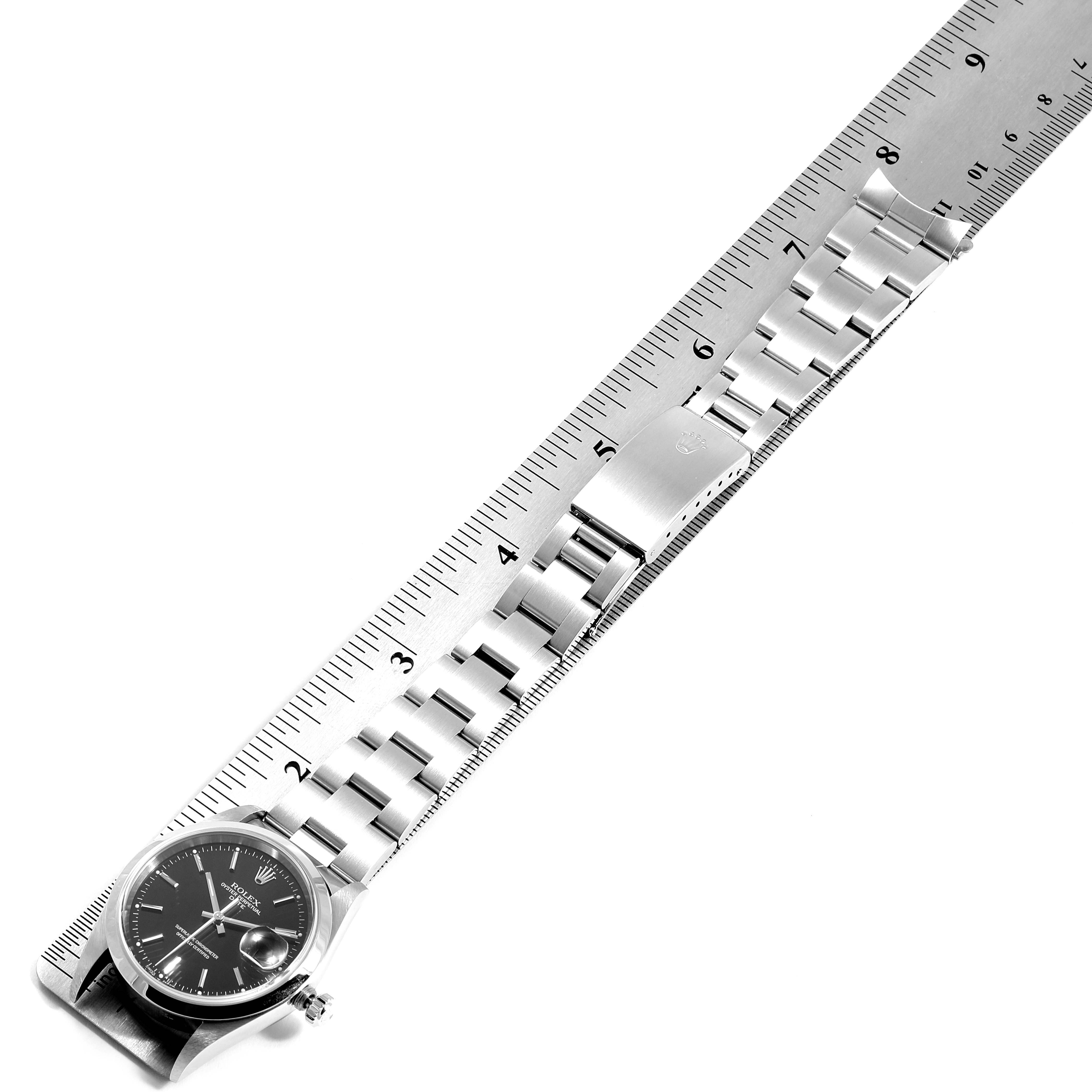 The image shows a Rolex Date 15200 Men's Stainless Steel Black Dial 15200 Men's Stainless Steel Black Dial model watch positioned diagonally next to a ruler, highlighting its clasp and bracelet.