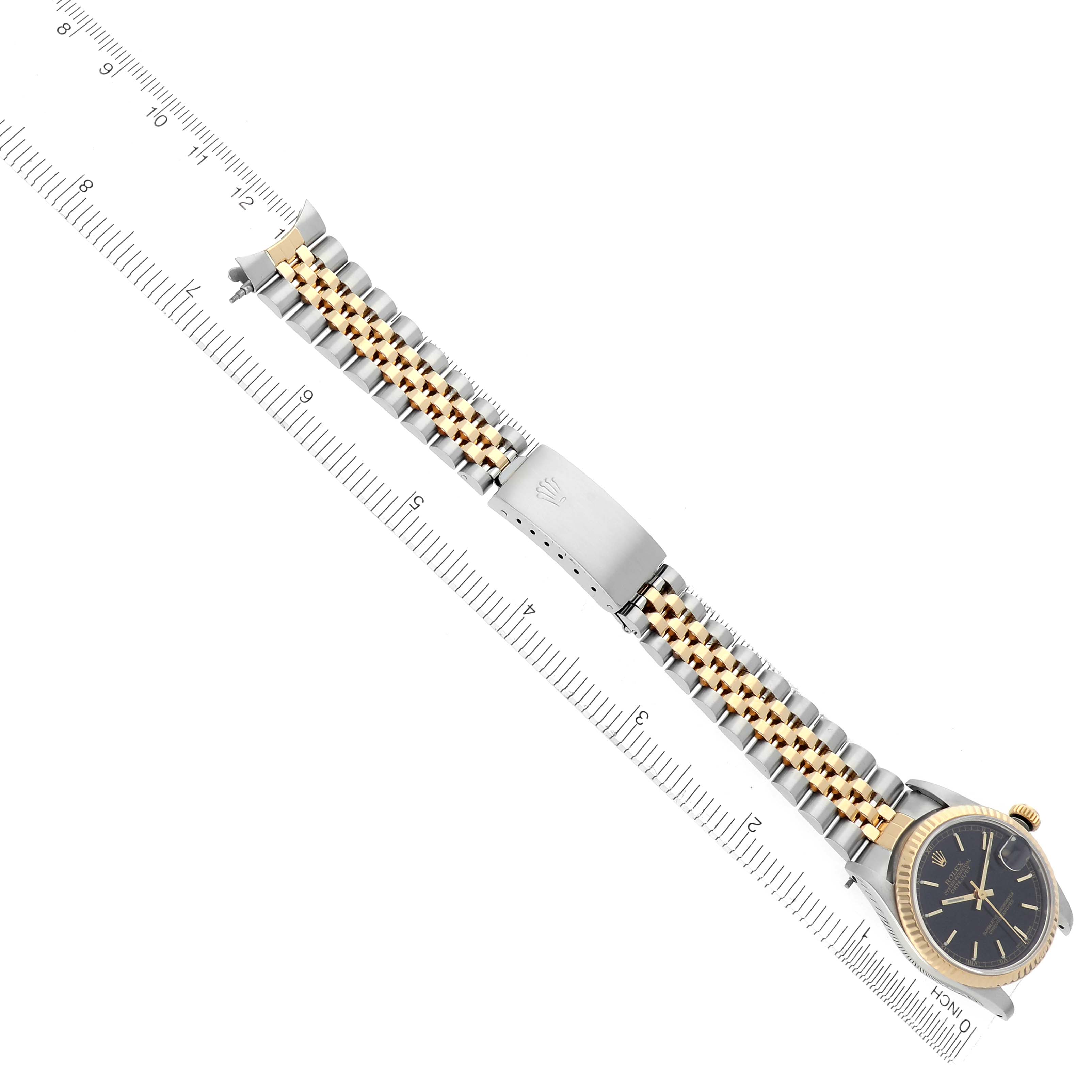 The Rolex Mid-Size 68273 Women
s Steel and Gold (two tone) Black Dial 68273 Women
s Steel and Gold (two tone) Black Dial watch is shown from a top view, displaying the face, full bracelet, and clasp alongside a ruler for scale.