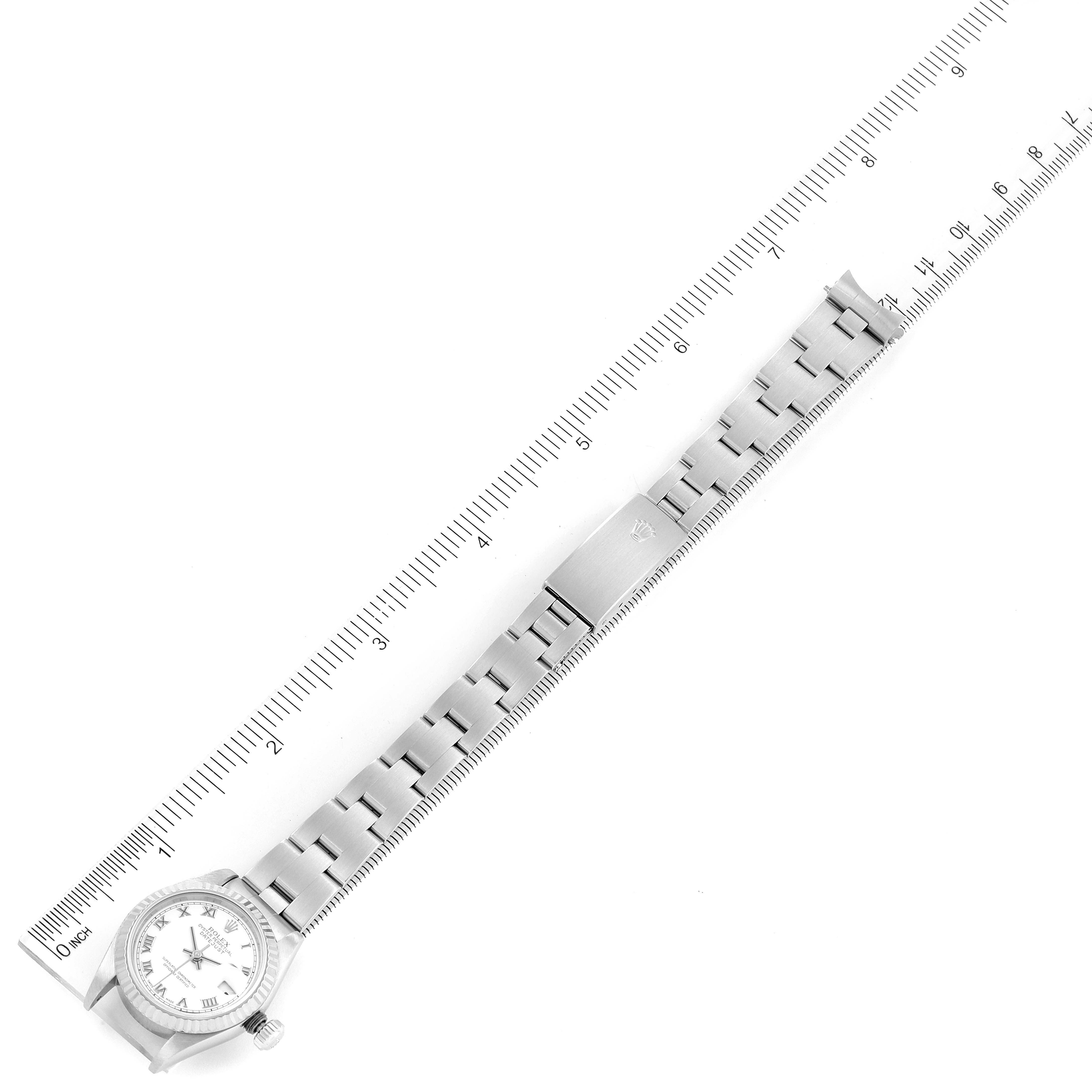This image shows a top-down view of a Rolex Datejust 79174 Women
s Stainless Steel White Dial 79174 Women
s Stainless Steel White Dial watch with its band laid out alongside a ruler for measurement.
