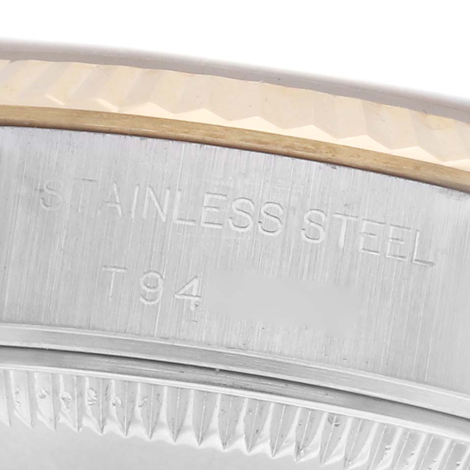 This close-up image shows the side of a Rolex Datejust 69173 Women
s Steel and Gold (two tone) Champagne Dial 69173 Women
s Steel and Gold (two tone) Champagne Dial
s bezel and case with "STAINLESS STEEL" and "T94" engraved.