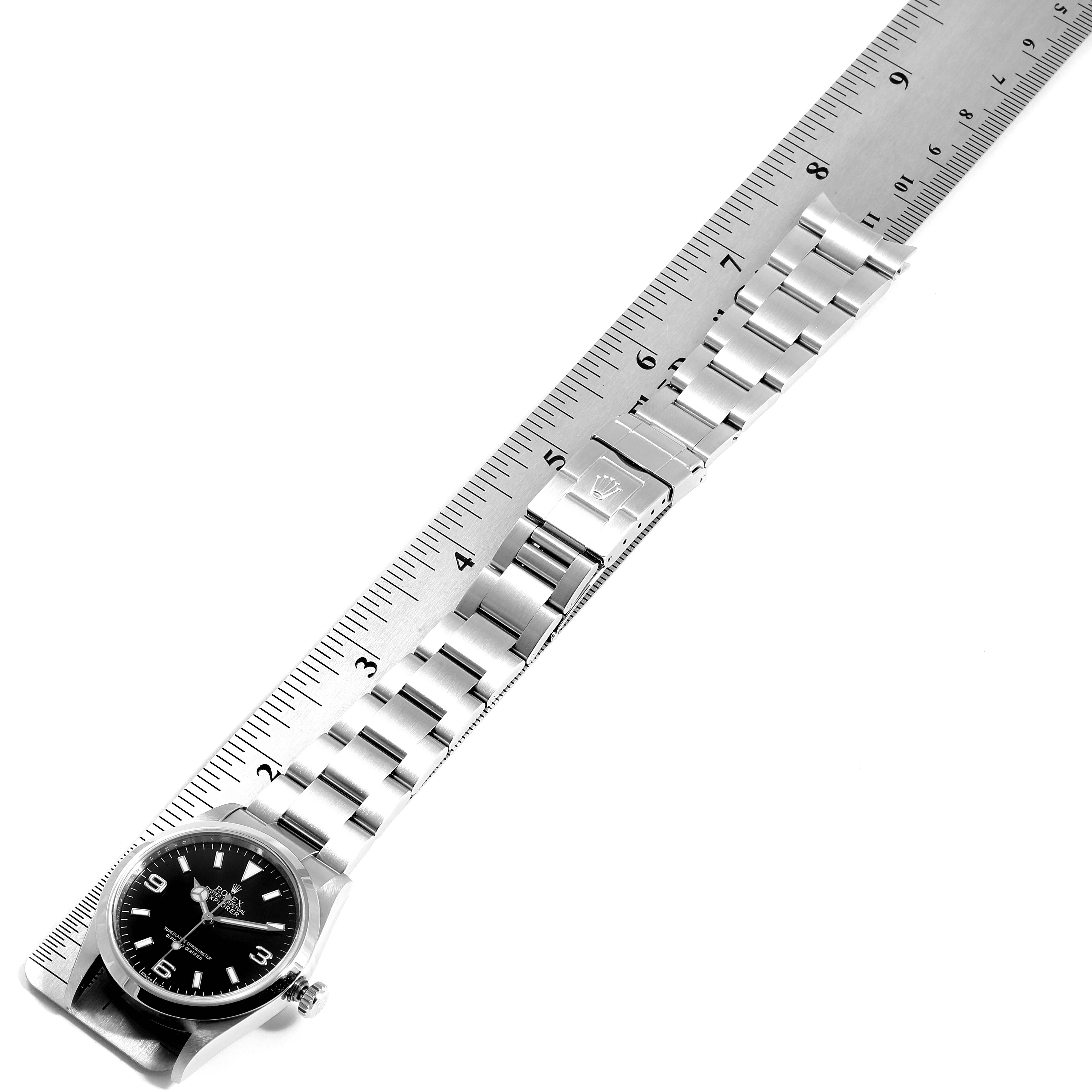 The Rolex Explorer 114270 Men
s Stainless Steel Black Dial 114270 Men
s Stainless Steel Black Dial watch is shown at a slight angle with its face, bracelet, and clasp visible alongside a ruler for scale.