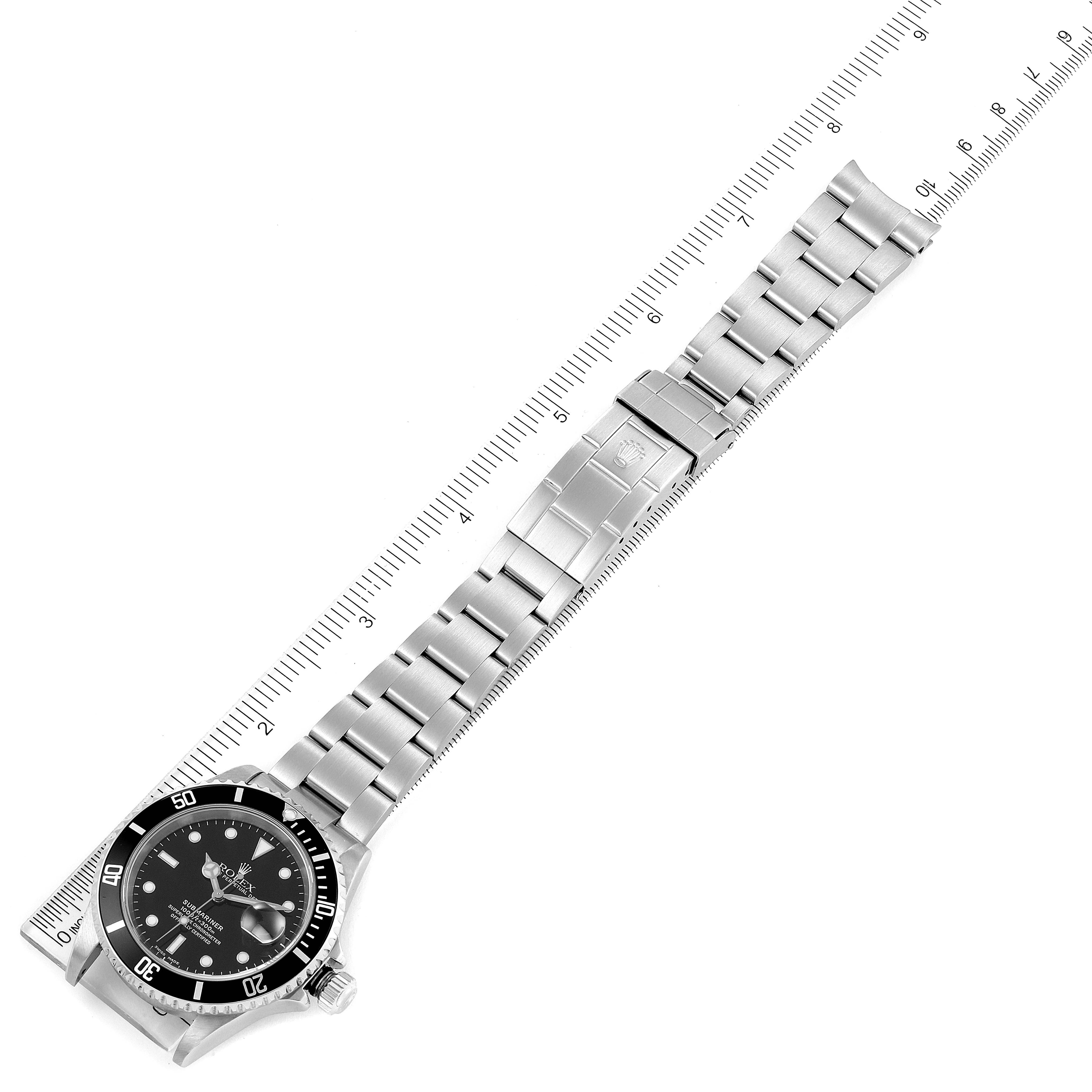 This image shows a Rolex Submariner 16610 Men
s Stainless Steel Black Dial 16610 Men
s Stainless Steel Black Dial watch laid out flat alongside a ruler, highlighting its band and face.