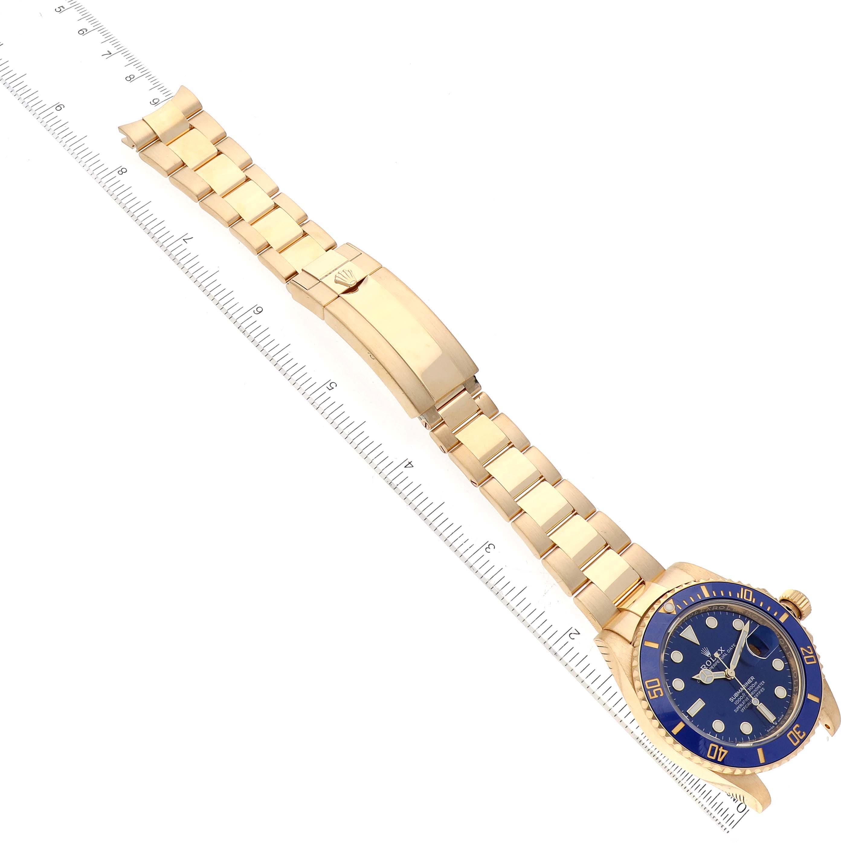 The image shows a top view of a Rolex Submariner 126618LB Men's Yellow Gold Blue Dial 126618LB Men's Yellow Gold Blue Dial watch with a blue dial and gold bracelet, alongside a ruler for scale.