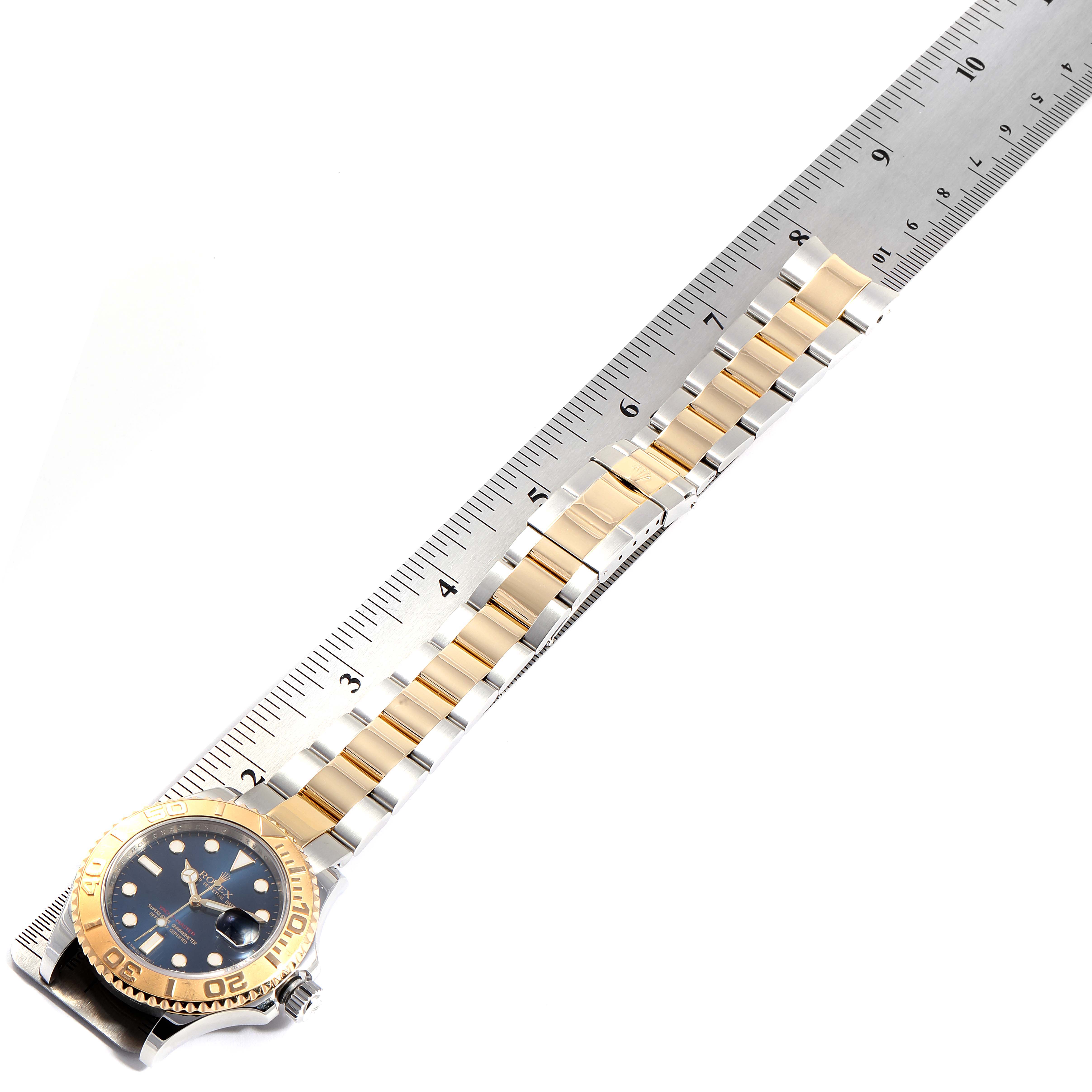 The image shows the Rolex Yacht-Master 16623 Men
s Steel and Gold (two tone) Blue Dial 16623 Men
s Steel and Gold (two tone) Blue Dial with a metal bracelet next to a ruler, viewed from an overhead angle.