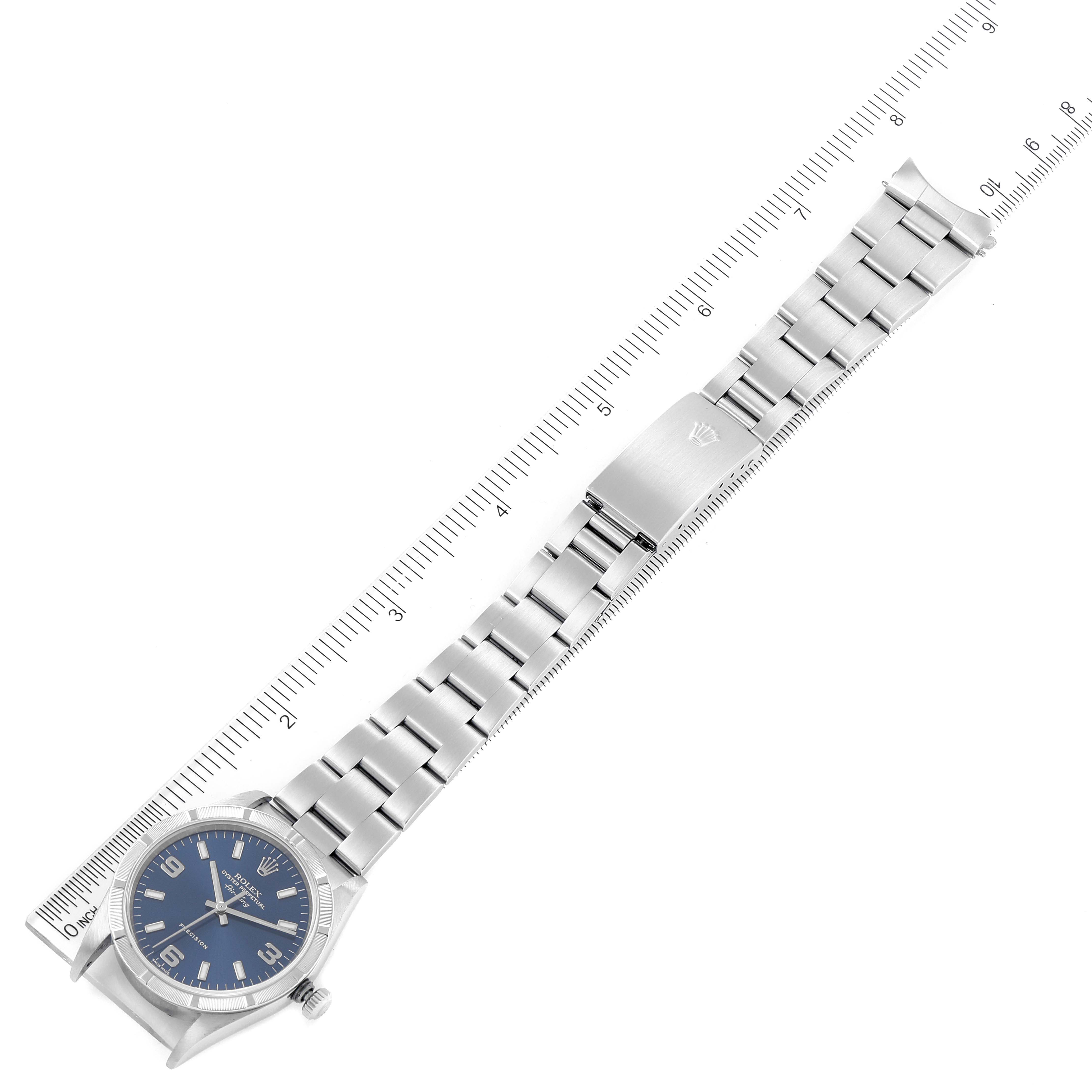 The Rolex Air-King 14010 Men's Stainless Steel Blue Dial 14010 Men's Stainless Steel Blue Dial watch is shown from an overhead angle, displaying the face, bracelet, and clasp alongside a measuring instrument.