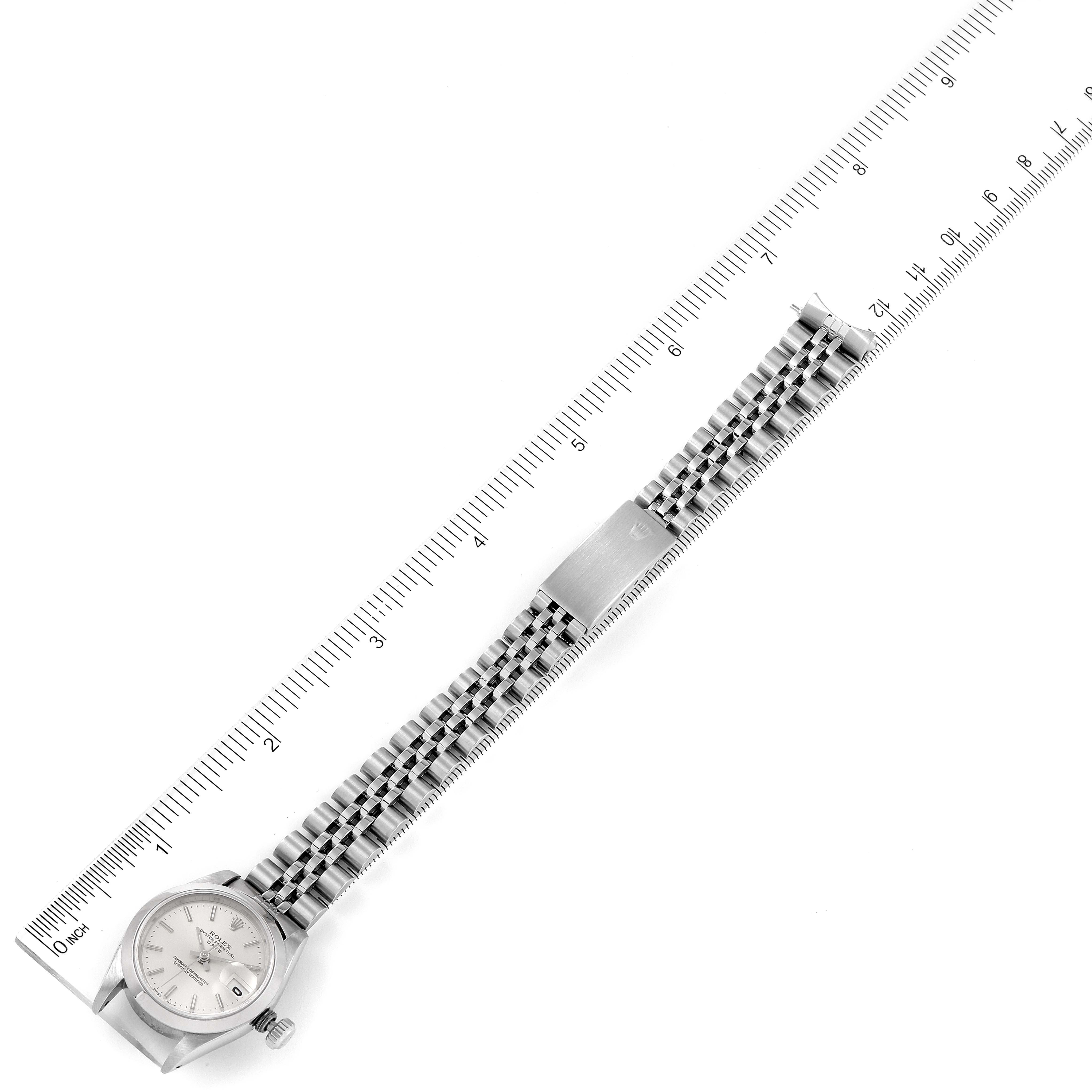 The image shows a top-down view of a Rolex Date 69160 Women
s Stainless Steel Silver Dial 69160 Women
s Stainless Steel Silver Dial model watch, its face, and bracelet alongside a ruler for scale.