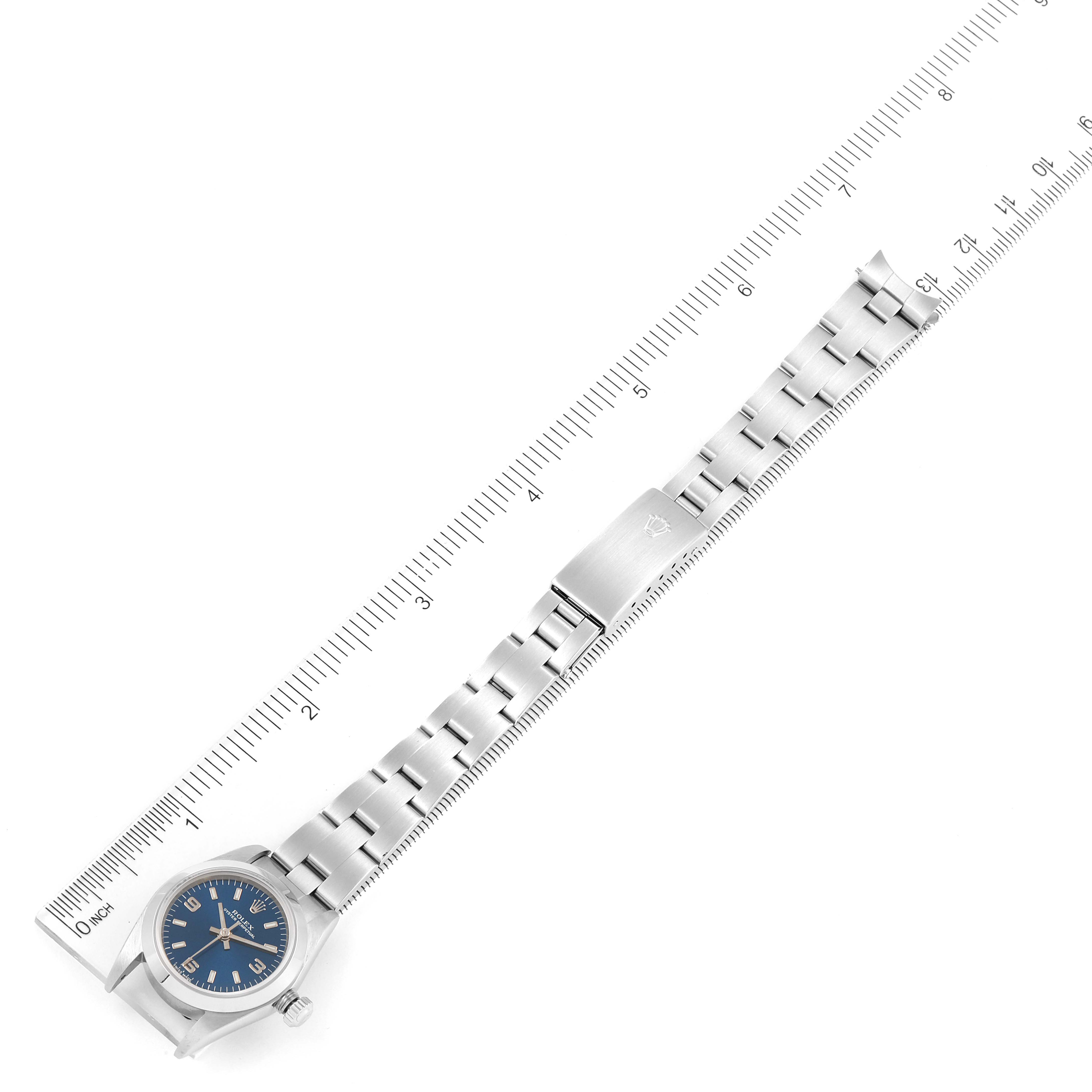 This image shows a top-down view of a Rolex Oyster Perpetual 76080 Women
s Stainless Steel Blue Dial 76080 Women
s Stainless Steel Blue Dial watch with a blue dial and a stainless steel bracelet next to a ruler.