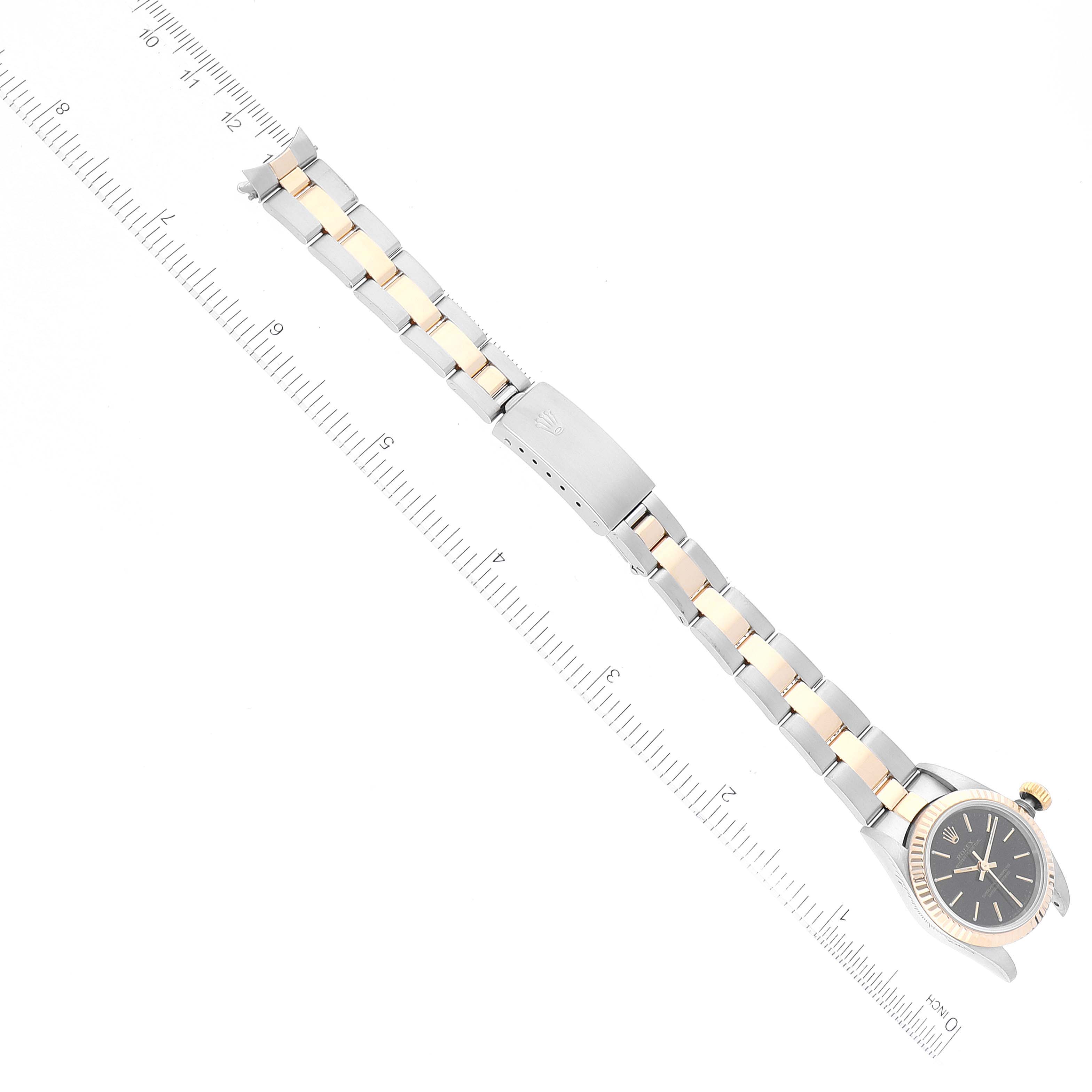 The image shows a top-down view of a Rolex Oyster Perpetual 67193 Women
s Steel and Gold (two tone) Black Dial 67193 Women
s Steel and Gold (two tone) Black Dial watch, highlighting its face, bracelet, and clasp, next to a ruler for scale.