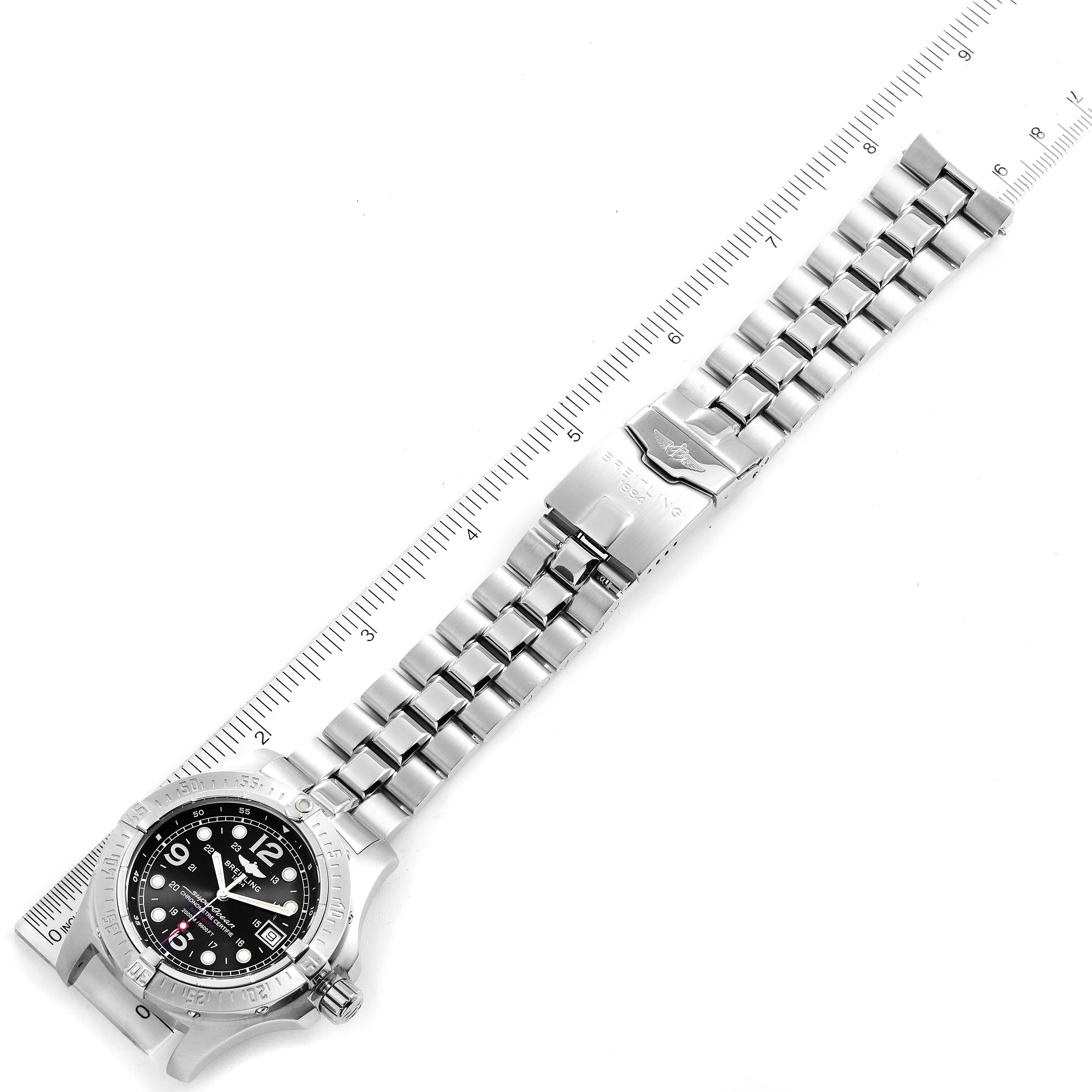 The image shows a Breitling Superocean A17390 Men
s Stainless Steel Black Dial A17390 Men
s Stainless Steel Black Dial watch at an overhead angle, displaying the face, bezel, and full metal bracelet with a ruler for scale.