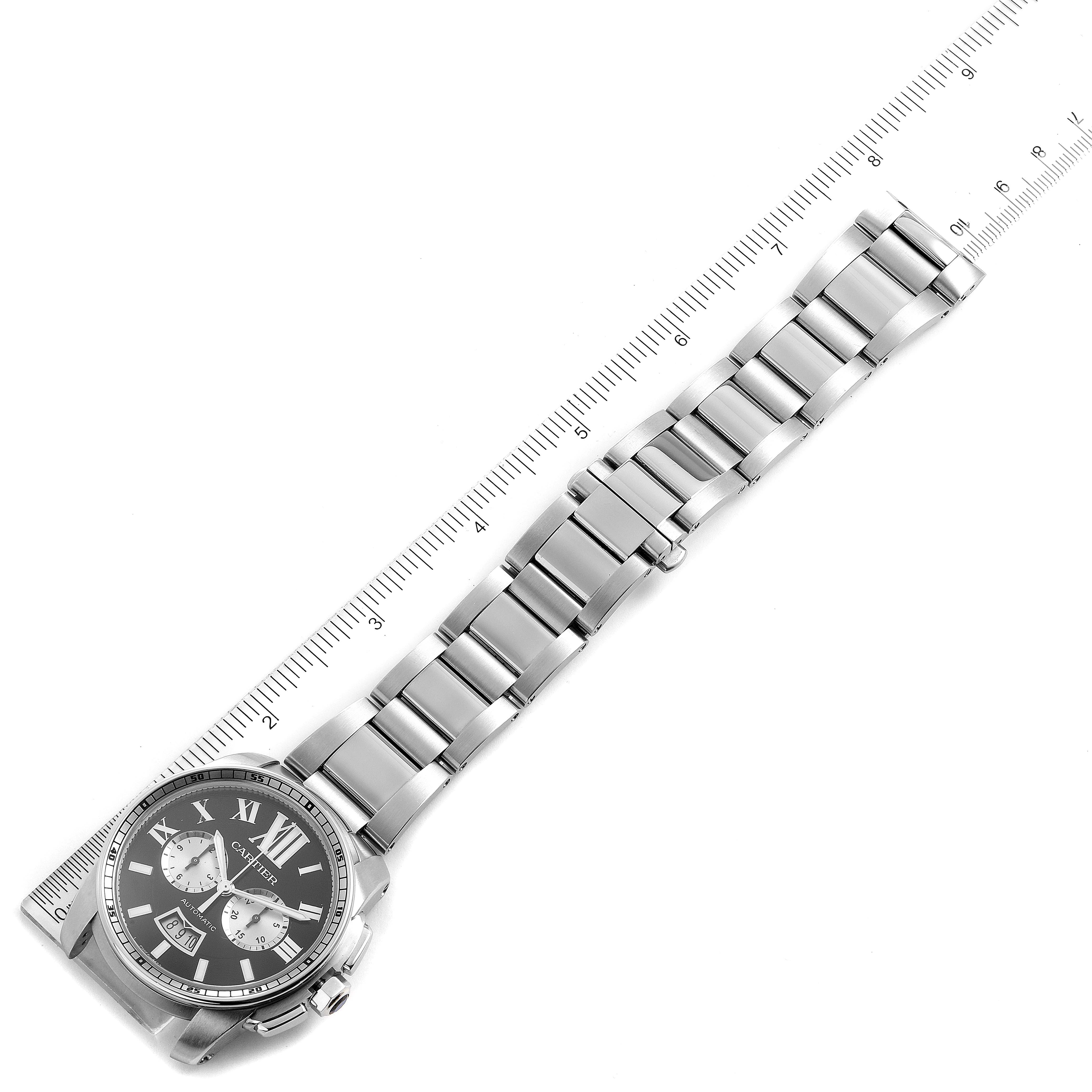 The image shows a top-down view of the Calibre de Cartier watch by Cartier, highlighting the face and full metal band next to a ruler.