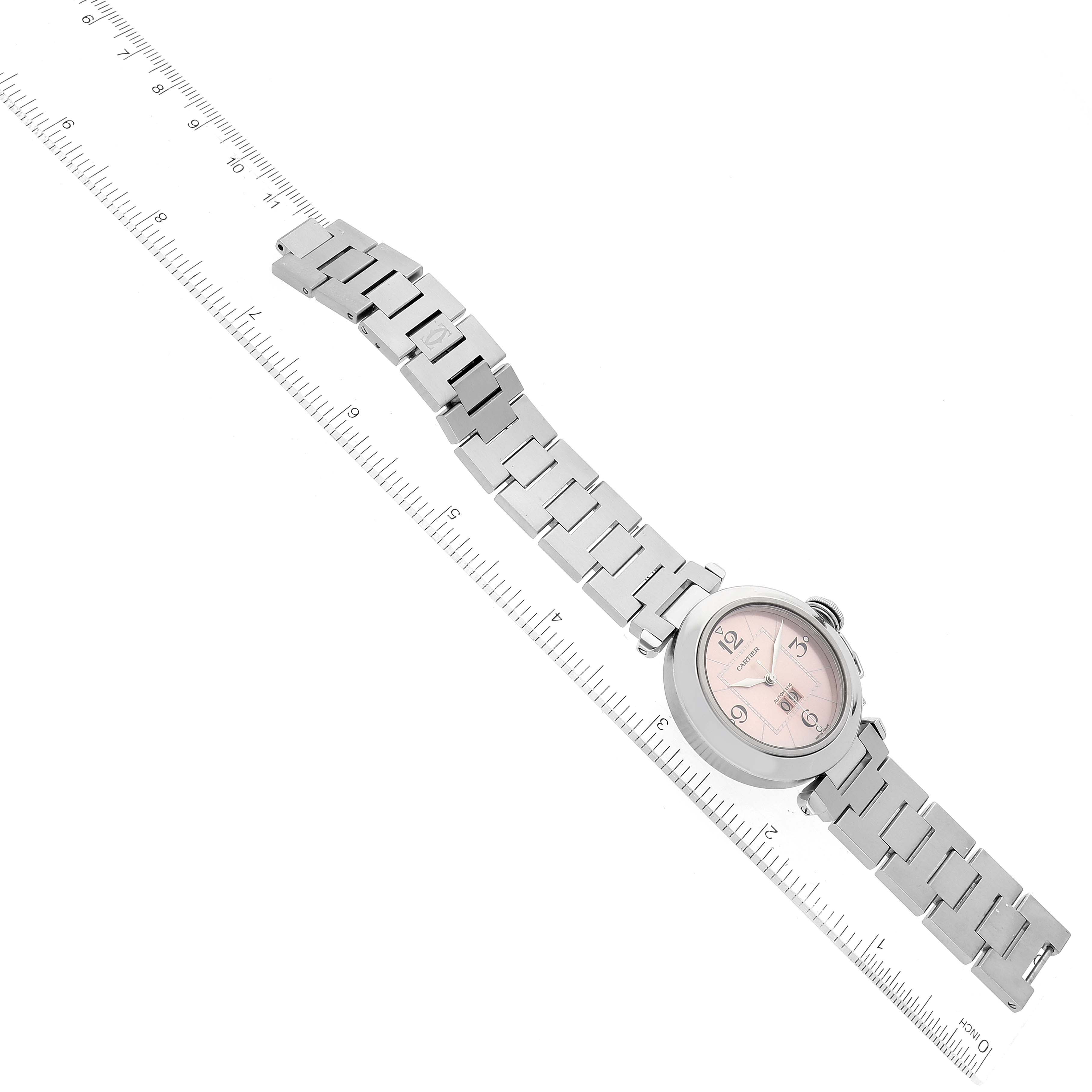 The Cartier Pasha W31058M7 Men's Stainless Steel Pink Dial W31058M7 Men's Stainless Steel Pink Dial watch is shown flat with its full bracelet and pink dial face visible, against a ruler for scale.