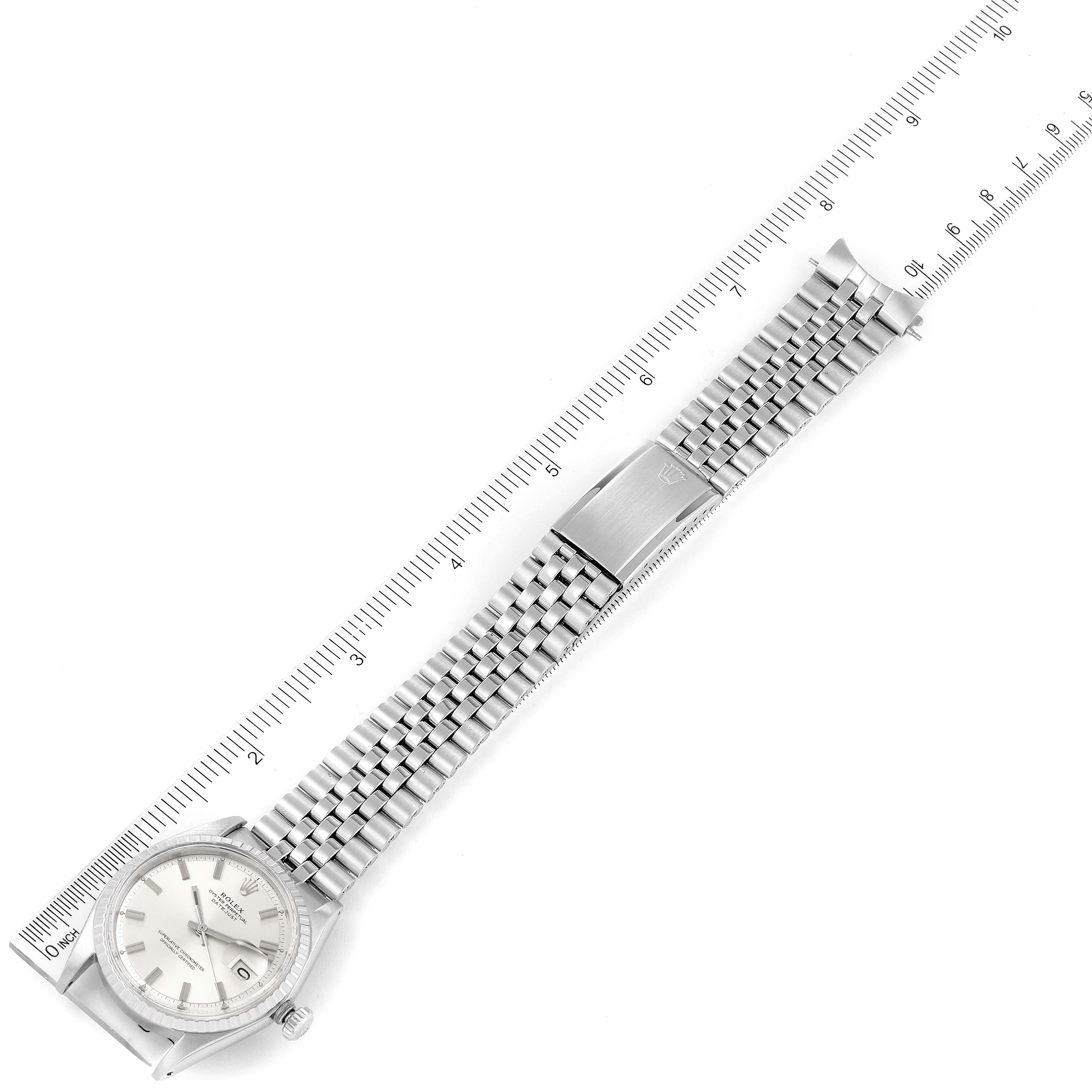 The image shows a top-down view of a Rolex Vintage Collection 1603 Men
s Stainless Steel Silver Dial 1603 Men
s Stainless Steel Silver Dial watch with its face and entire metal strap laid flat along a ruler.