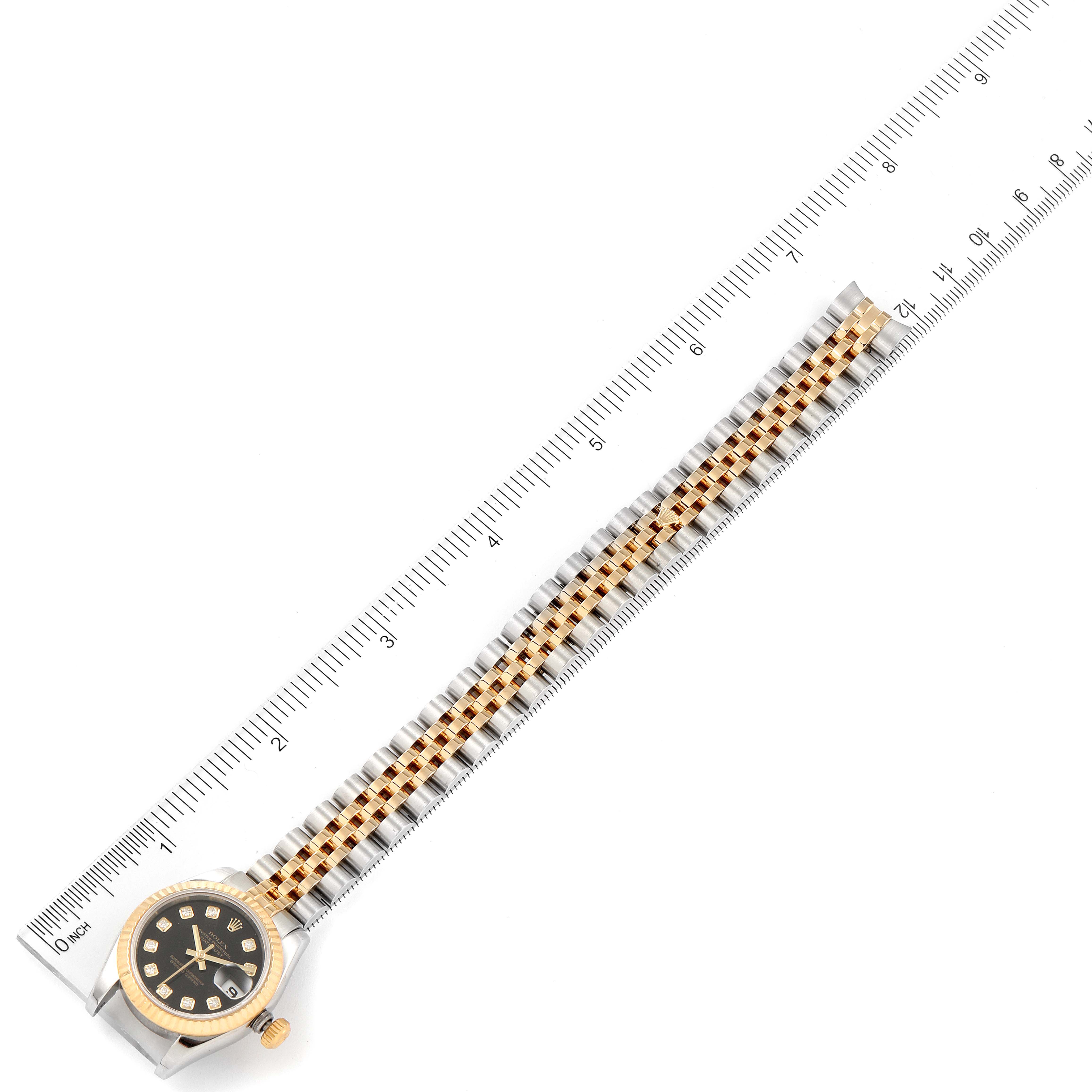 The image shows a Rolex Datejust 179173 Women's Steel and Gold (two tone) Black Dial 179173 Women's Steel and Gold (two tone) Black Dial watch laid flat with its bracelet aligned next to a ruler for scale.
