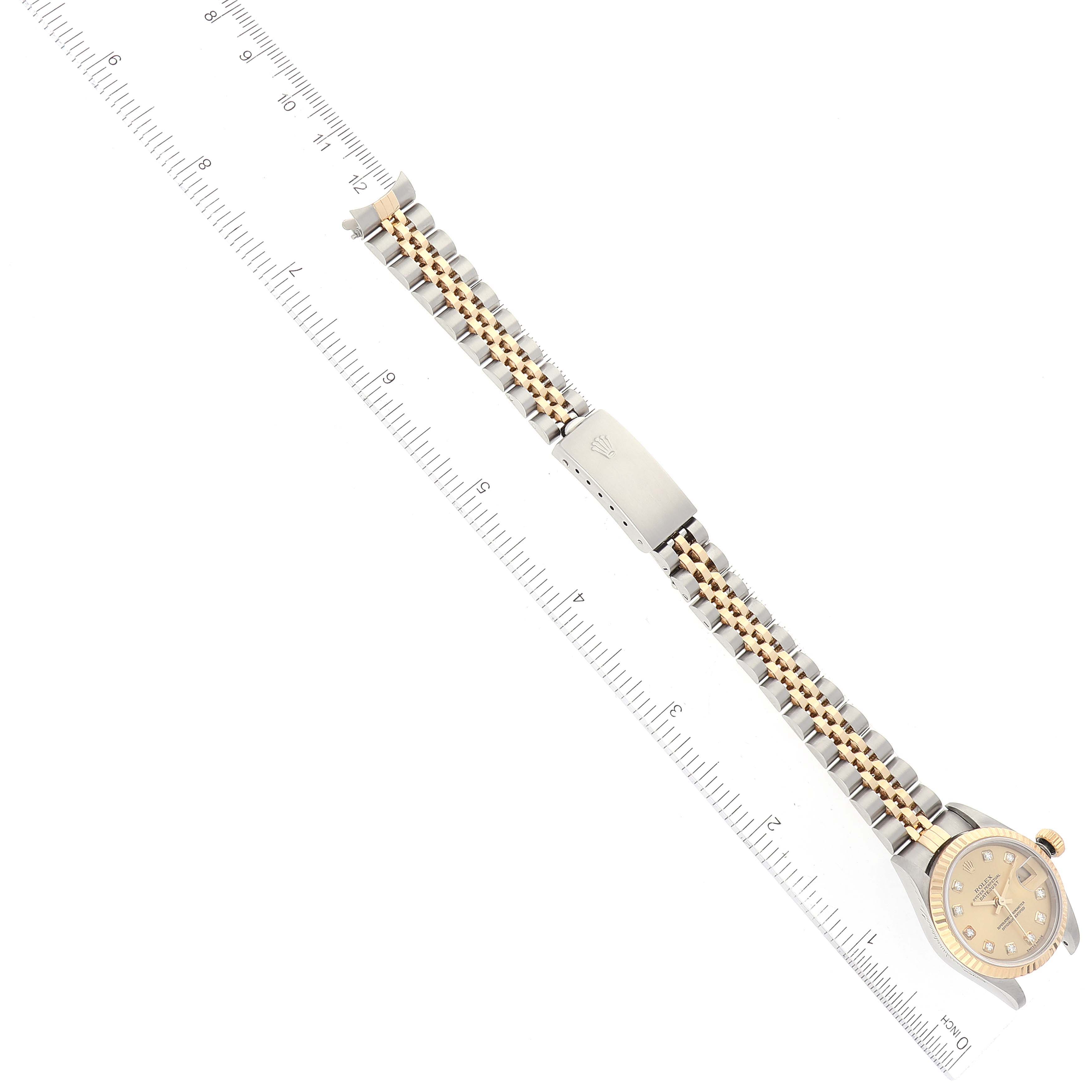 This image shows the Rolex Datejust 79173 Women's Steel and Gold (two tone) Champagne Dial 79173 Women's Steel and Gold (two tone) Champagne Dial watch laid flat, showcasing its entire band alongside a ruler for scale.