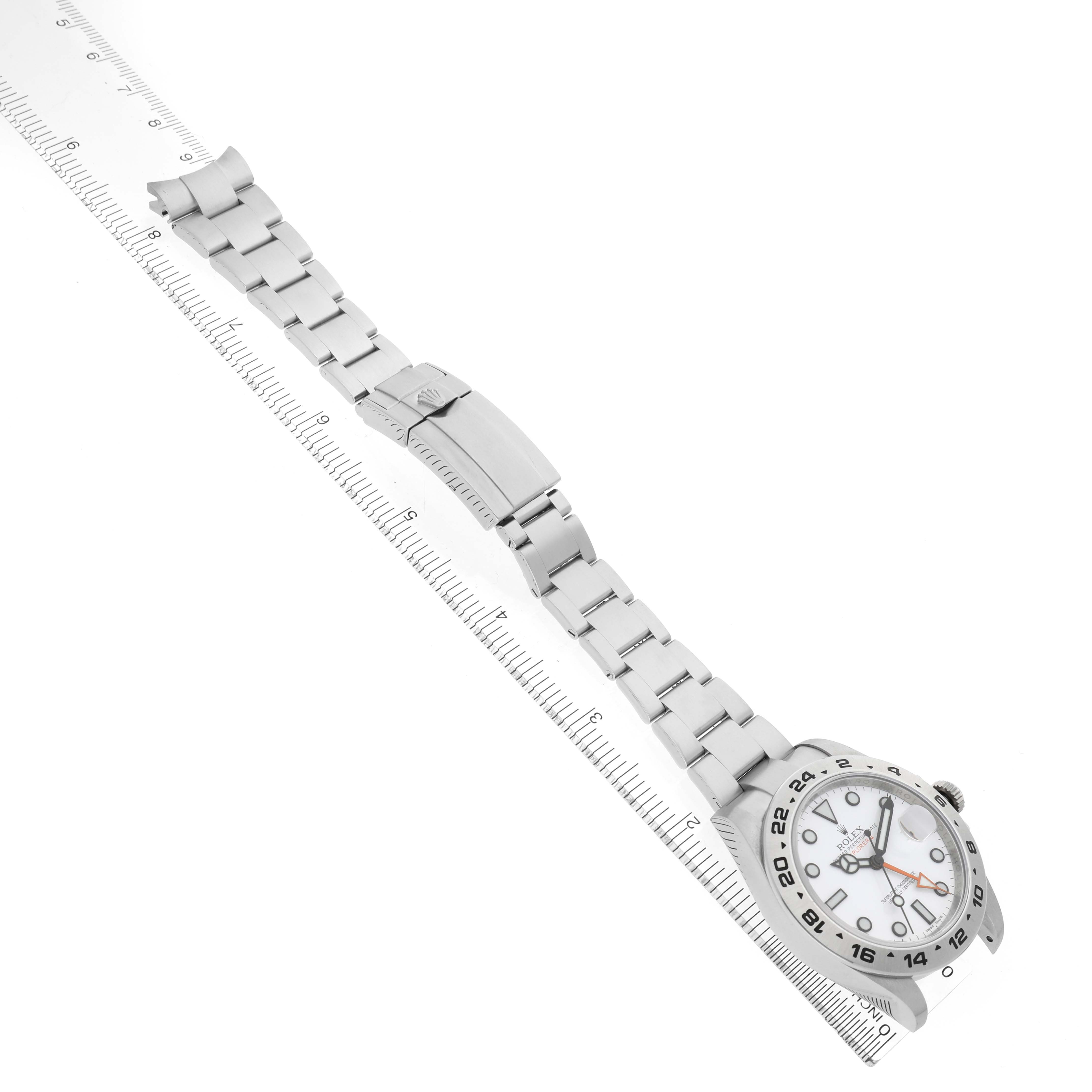 The Rolex Explorer 216570 Men's Stainless Steel White Dial watch is shown from a top-down angle, displaying the face, bezel, and full bracelet on a ruler.