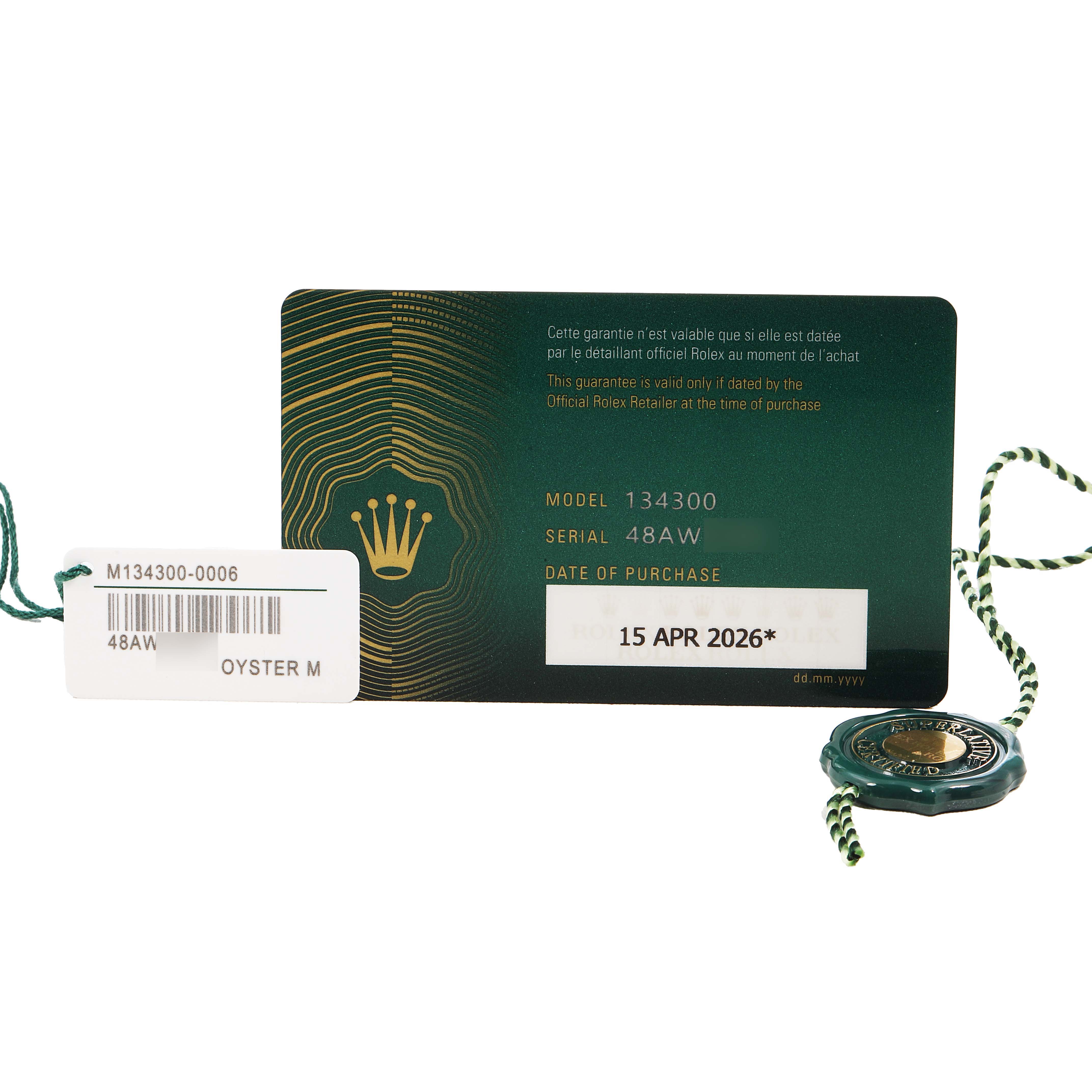 The image shows the warranty card and tags for a Rolex Oyster Perpetual 134300 Men's Stainless Steel Green Dial model, including serial and model numbers.