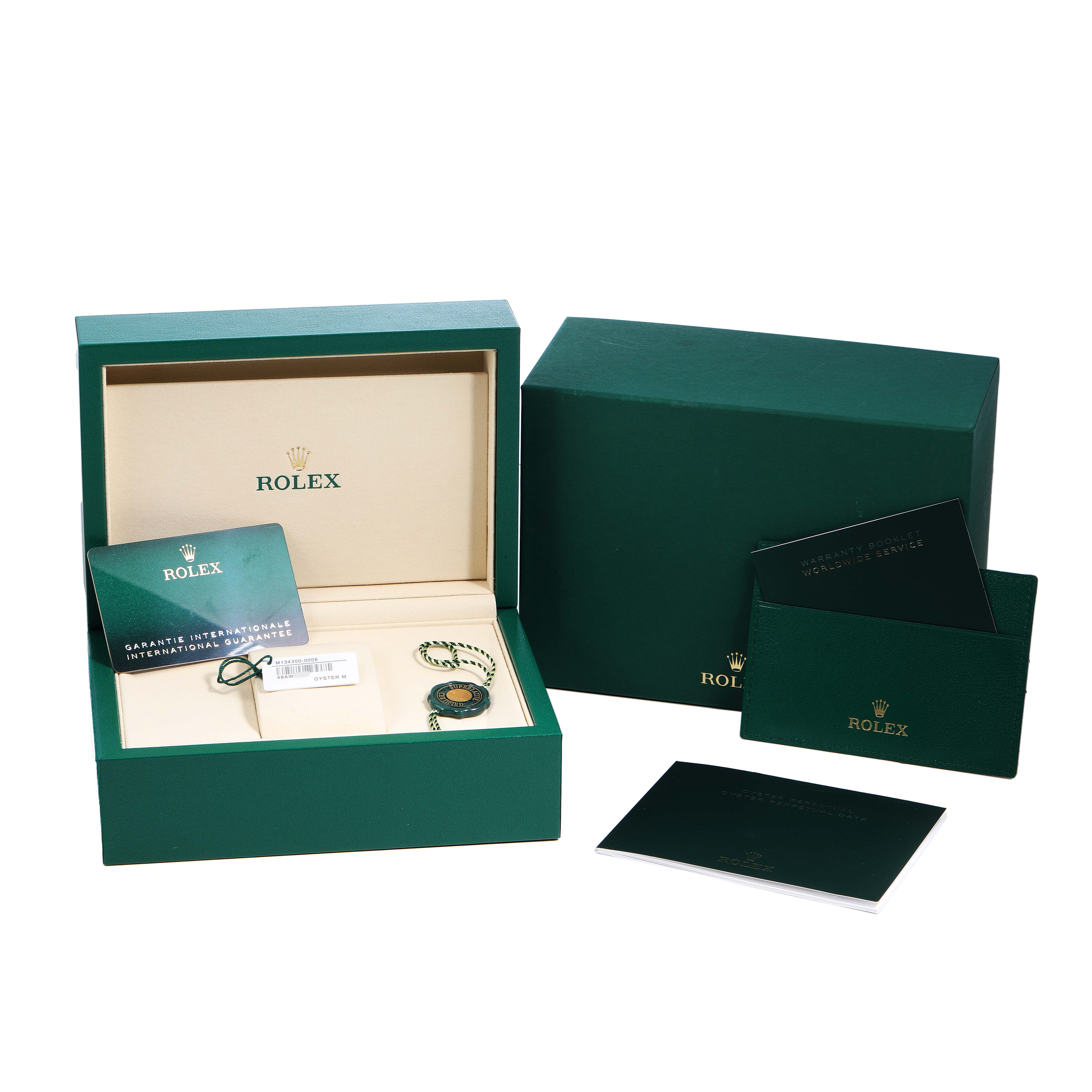 The image displays the packaging and accessories of a Rolex Oyster Perpetual 134300 Men's Stainless Steel Green Dial, showing the box, warranty card, booklet, and tag.