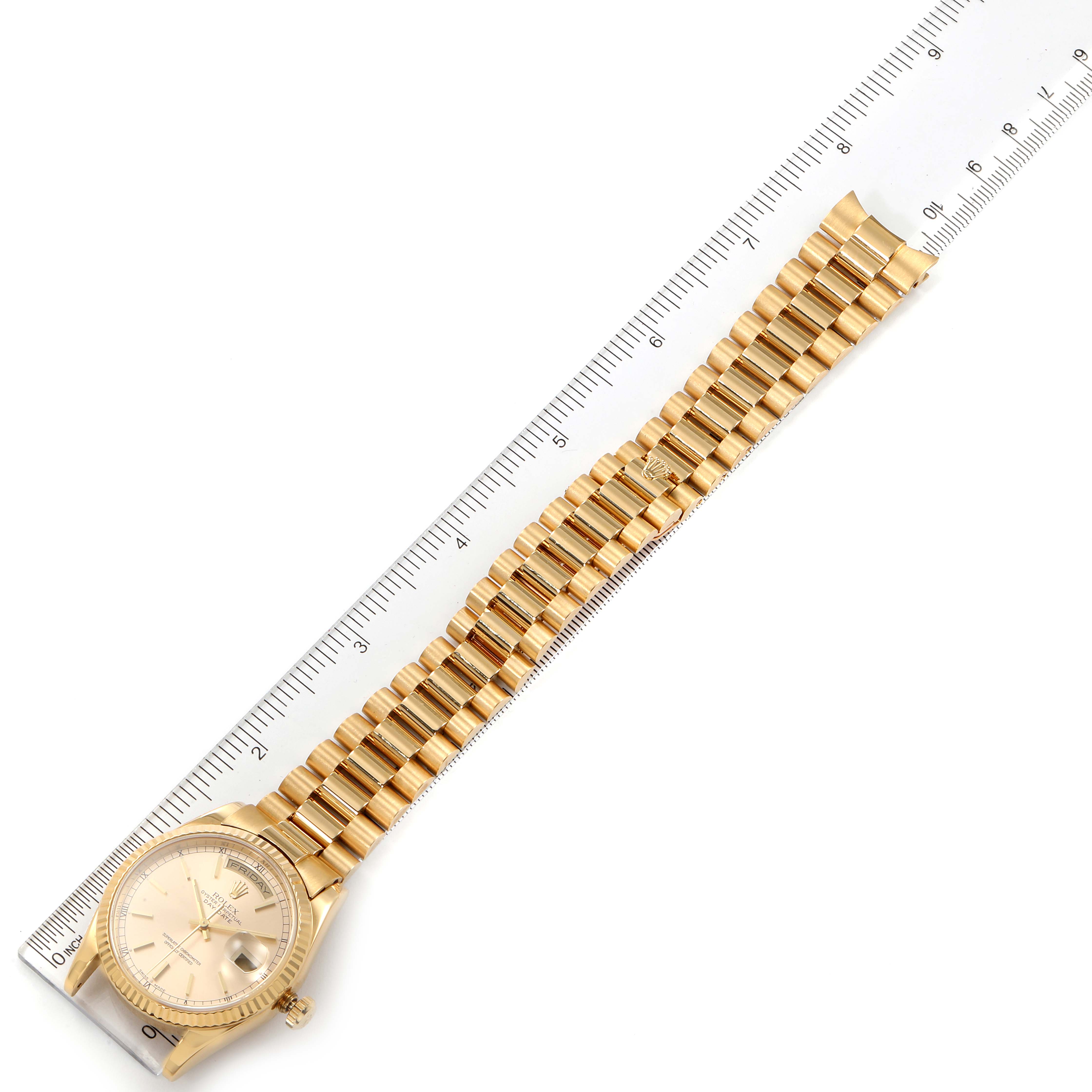 The image shows a Rolex President 118238 Men
s Yellow Gold Champagne Dial 118238 Men
s Yellow Gold Champagne Dial model watch laid flat next to a ruler, showcasing its face and gold bracelet.