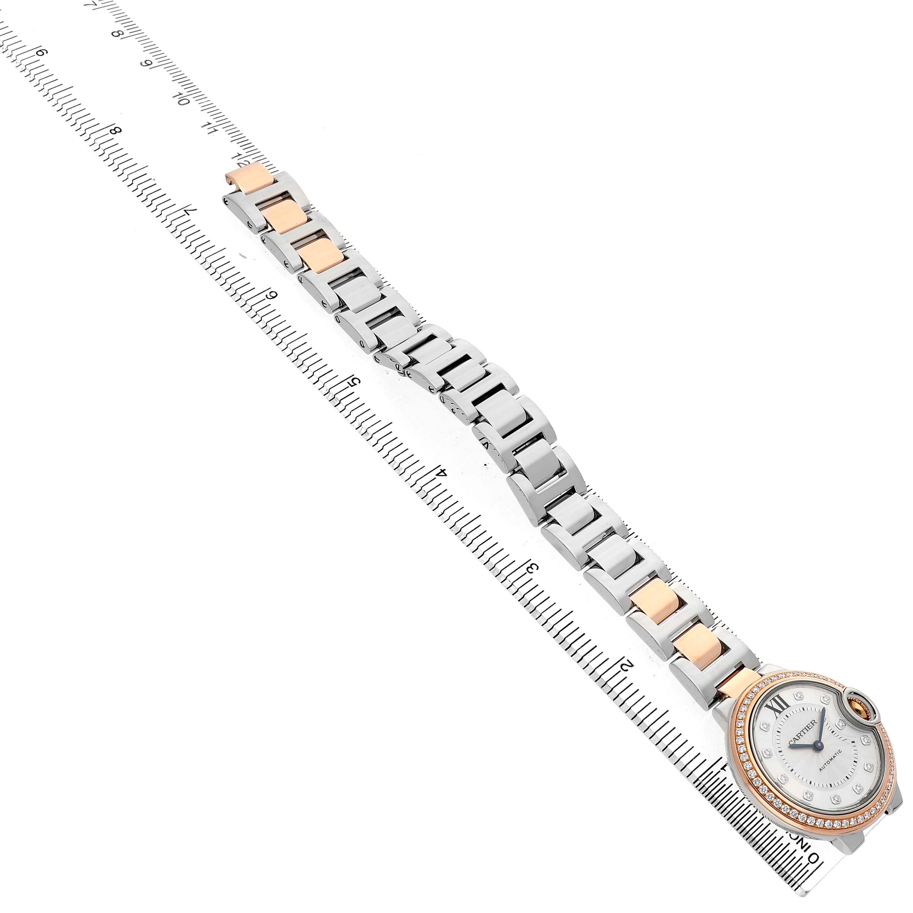 The Cartier Ballon Bleu WE902077 Women's Steel and Gold (two tone) Silver Dial watch is displayed face-up with a focus on its bracelet and diamond-encrusted bezel, placed alongside a ruler.