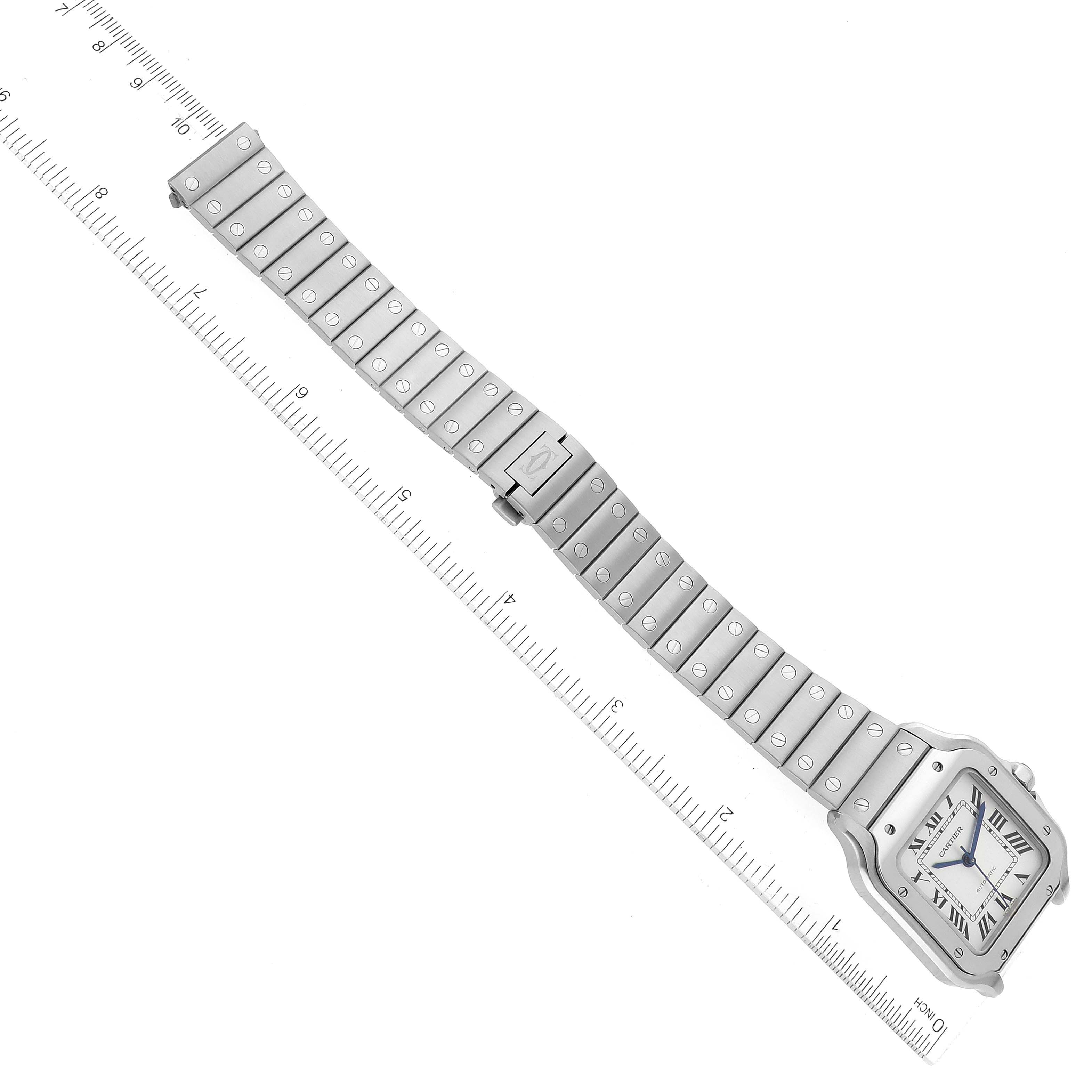 The Santos de Cartier watch is displayed flat, showing the face, case, and metal strap with a ruler for scale.