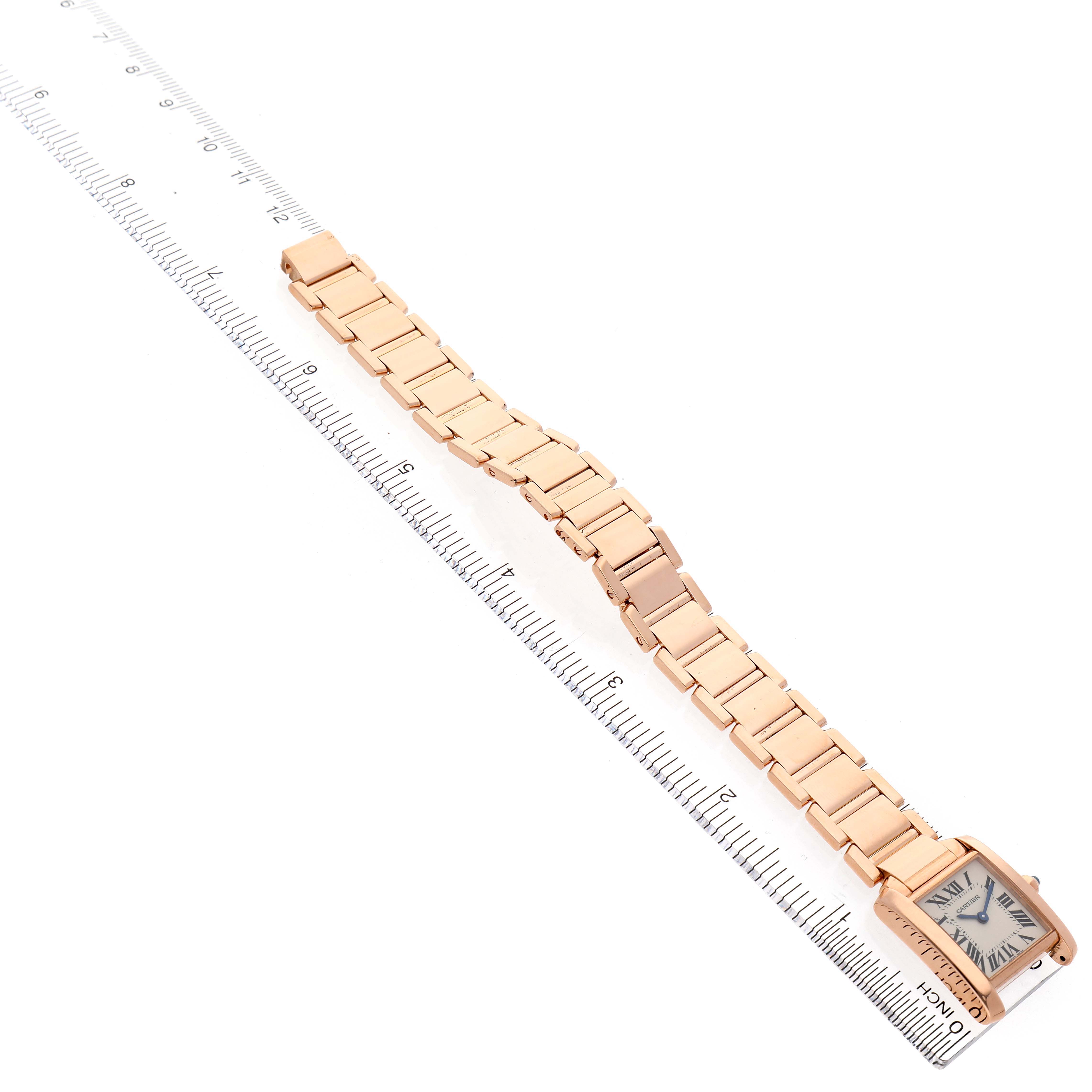 The Cartier Tank Française watch is shown from a top-down angle, displaying its face and full linked bracelet alongside a ruler.