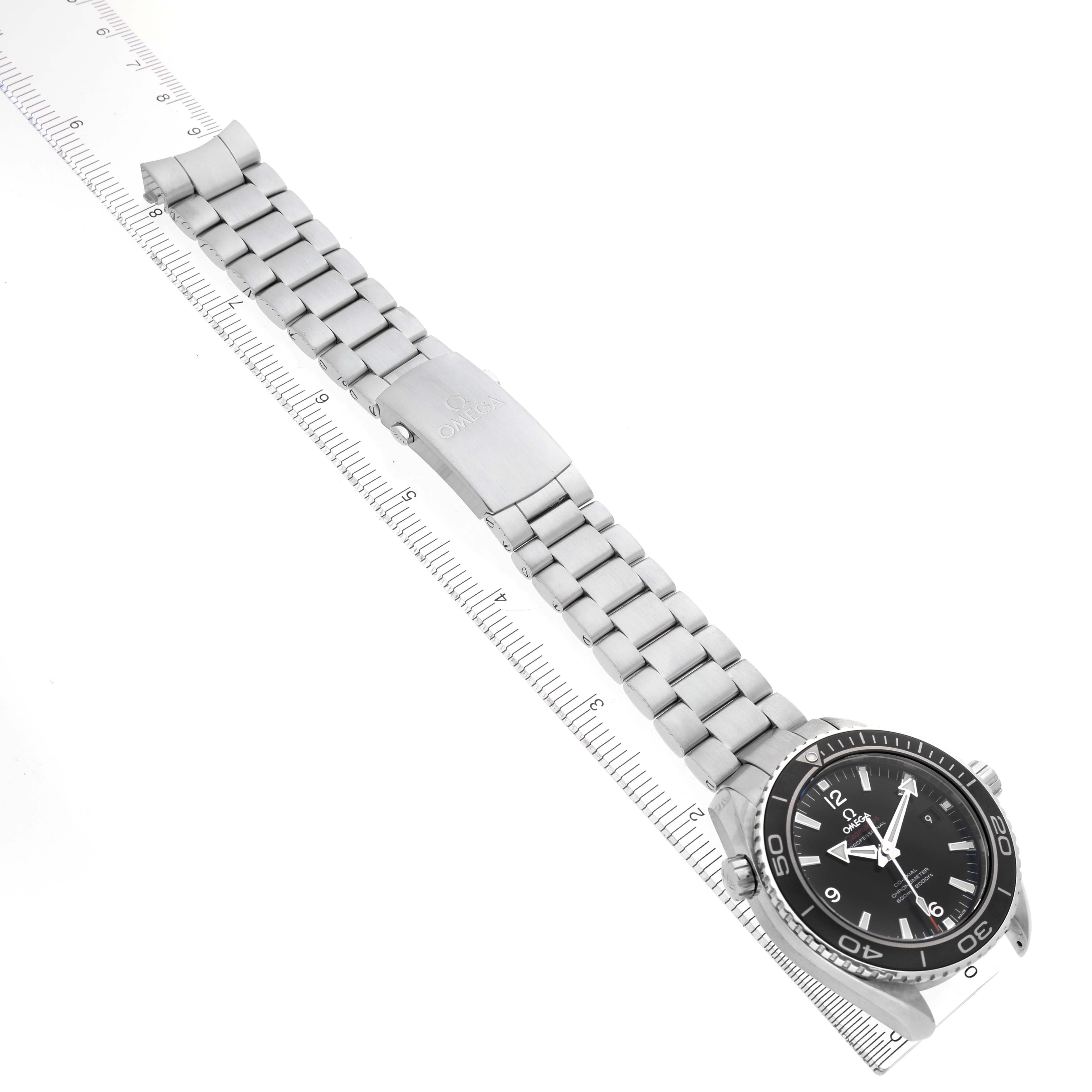 The Omega Planet Ocean 232.30.46.21.01.001 Men's Stainless Steel Black Dial watch is shown from a top view, highlighting the bracelet, clasp, and face with a ruler for scale.