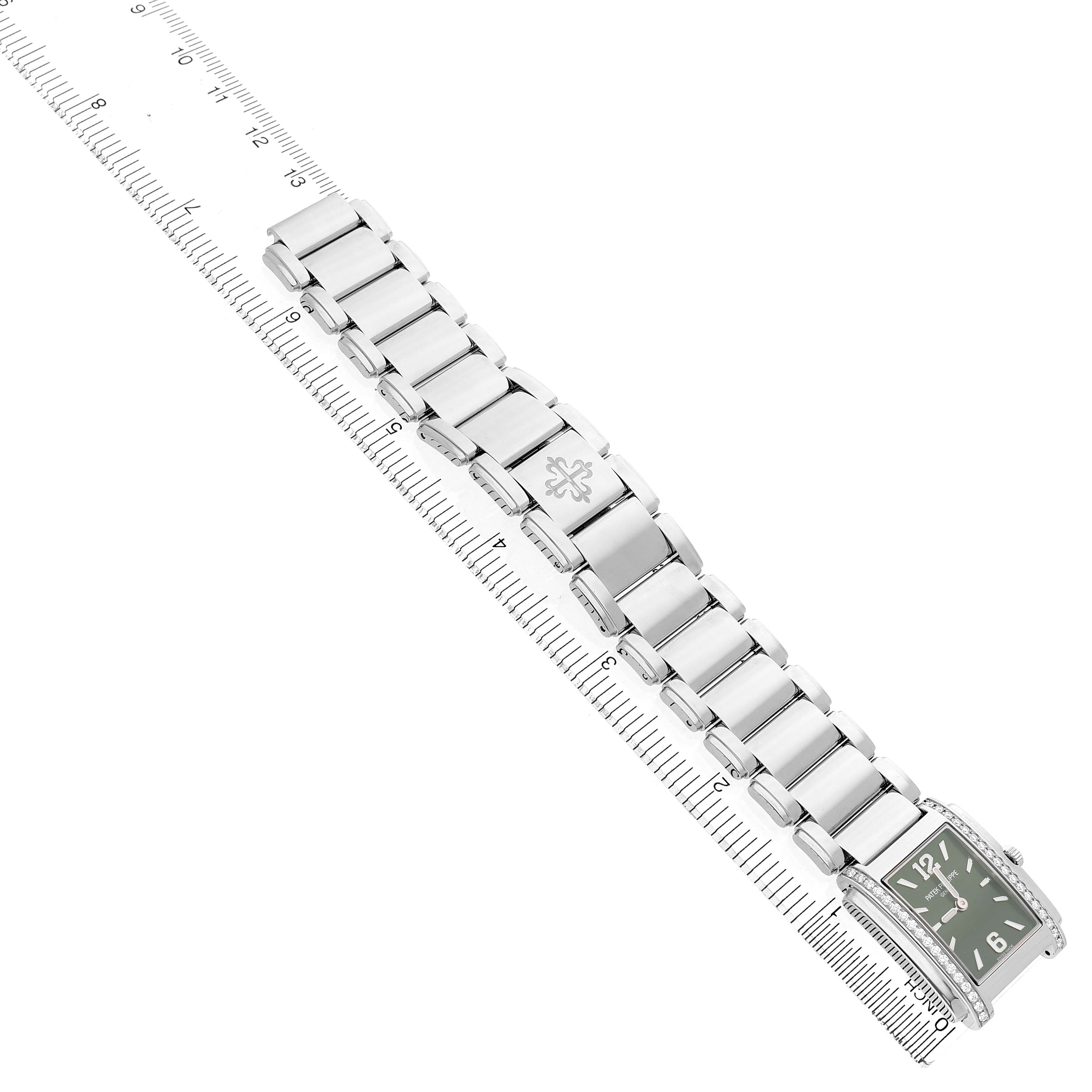 The Patek Philippe Twenty-4 4910A Women's Stainless Steel Green Dial watch is shown diagonally from above, highlighting its rectangular face and metal bracelet beside a ruler.