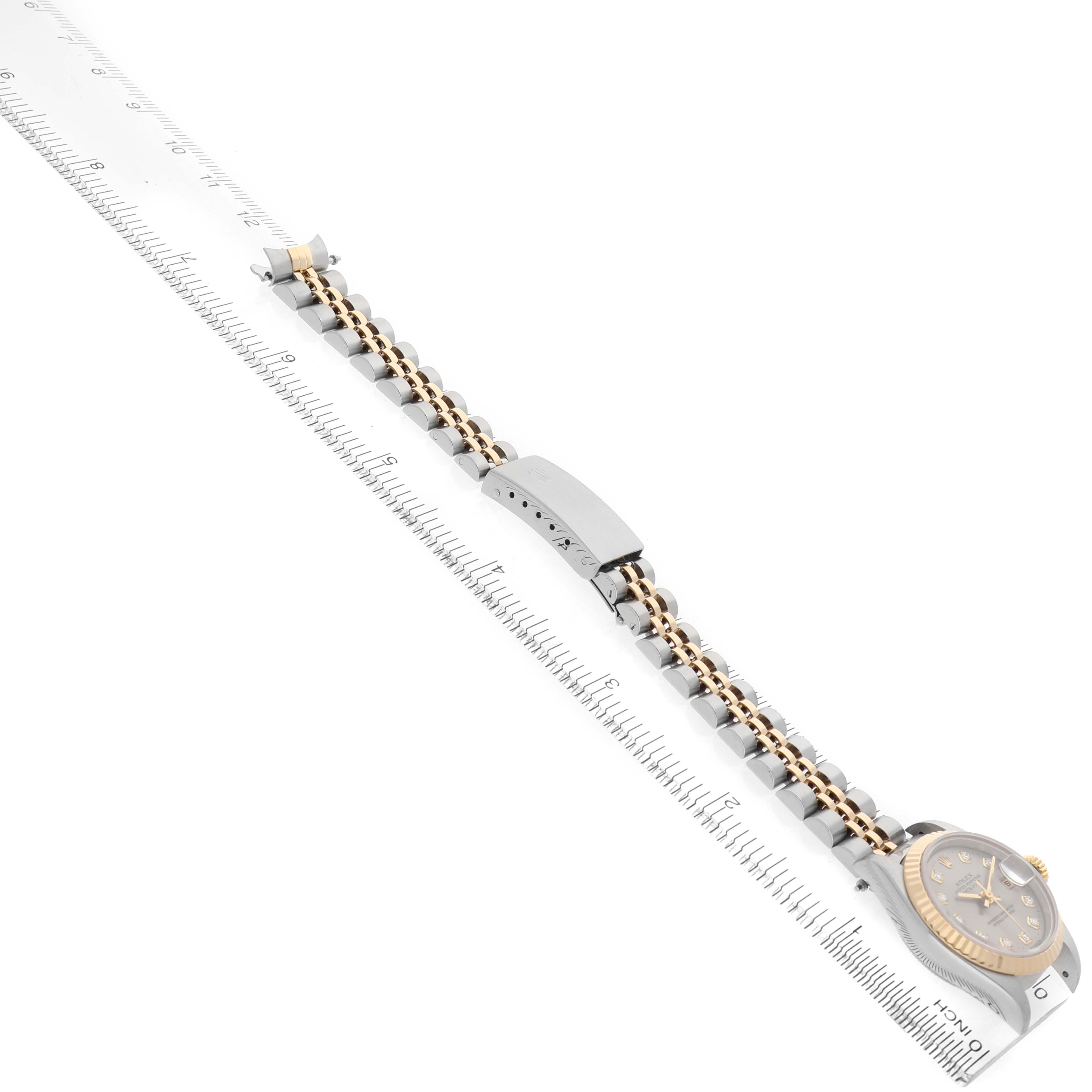 The image shows a Rolex Datejust 69173 Women's Steel and Gold (two tone) Silver Dial watch from a diagonal top-down angle, revealing the bracelet, clasp, and case next to a ruler.