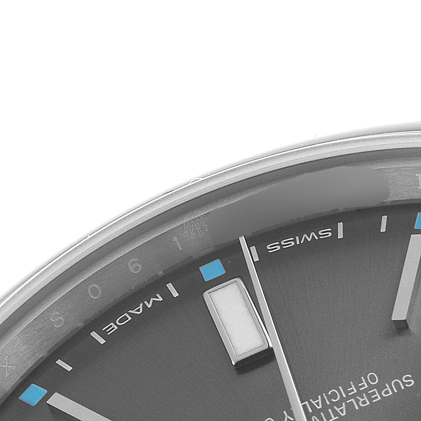 The image shows a close-up of the dial of a Rolex Oyster Perpetual 114300 Men's Stainless Steel Silver Dial 114300 Men's Stainless Steel Silver Dial watch, focusing on part of the hour markers and text.