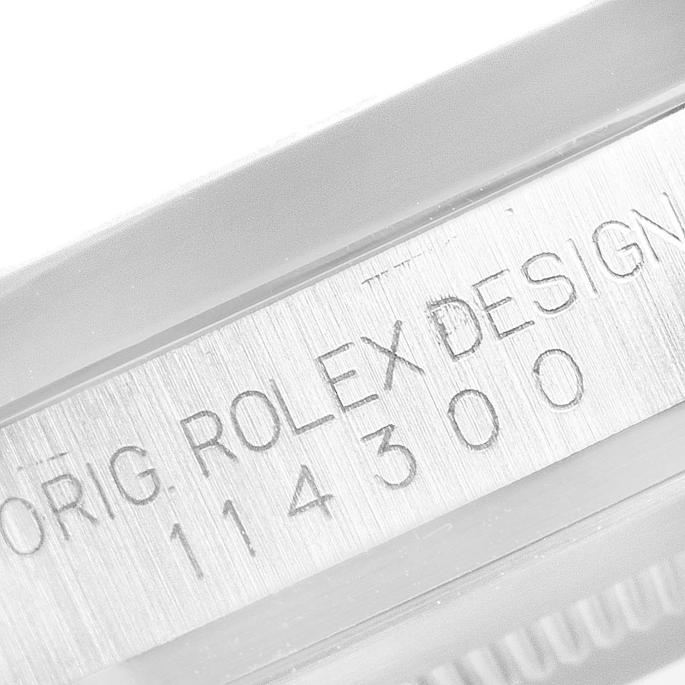 This image shows a close-up of the serial number and "Rolex Design" text on a Rolex Oyster Perpetual 114300 Men
s Stainless Steel Blue Dial 114300 Men
s Stainless Steel Blue Dial watch.