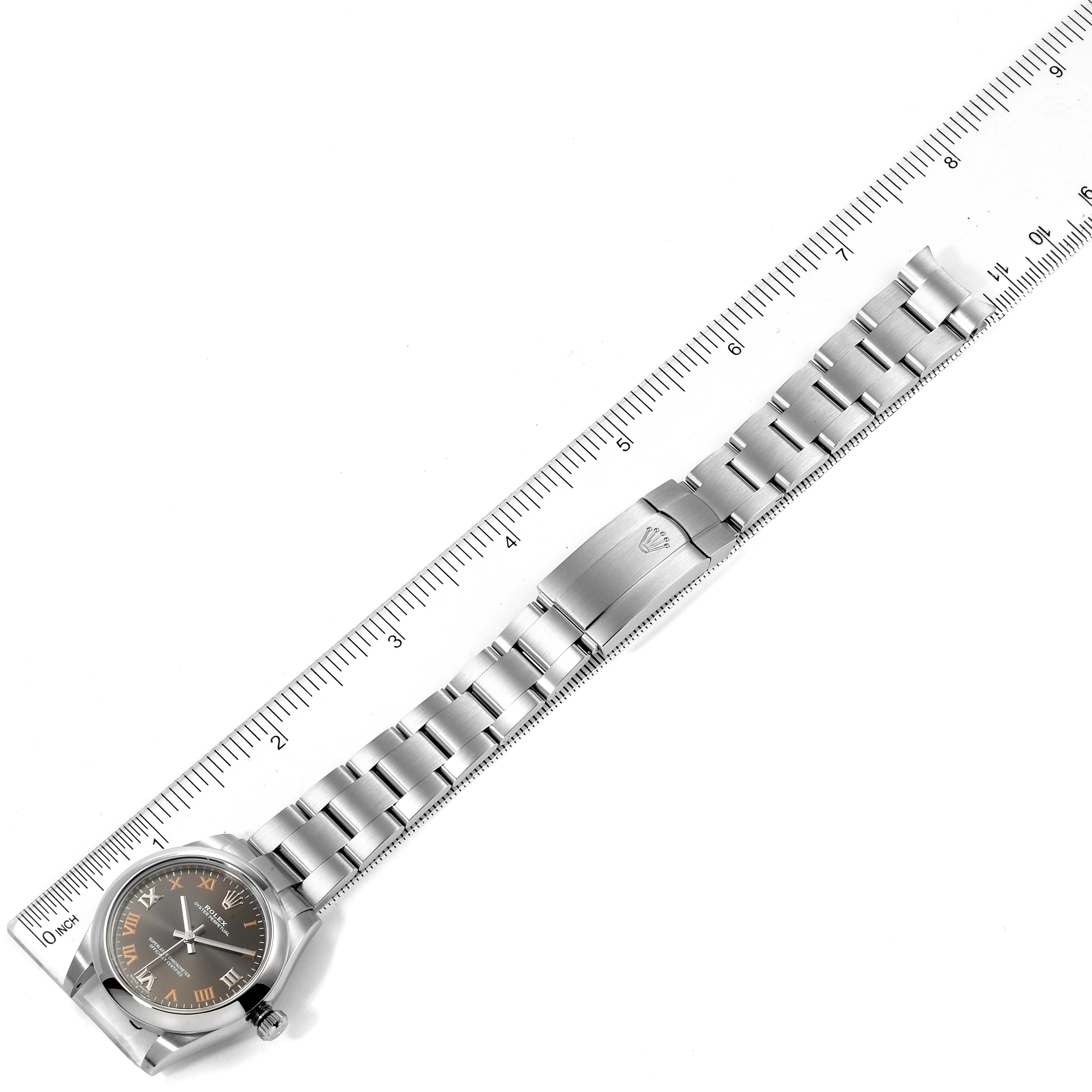 The Mid-Size Rolex watch is shown from a top-down angle with the watch face, bracelet, and clasp visible alongside a ruler.