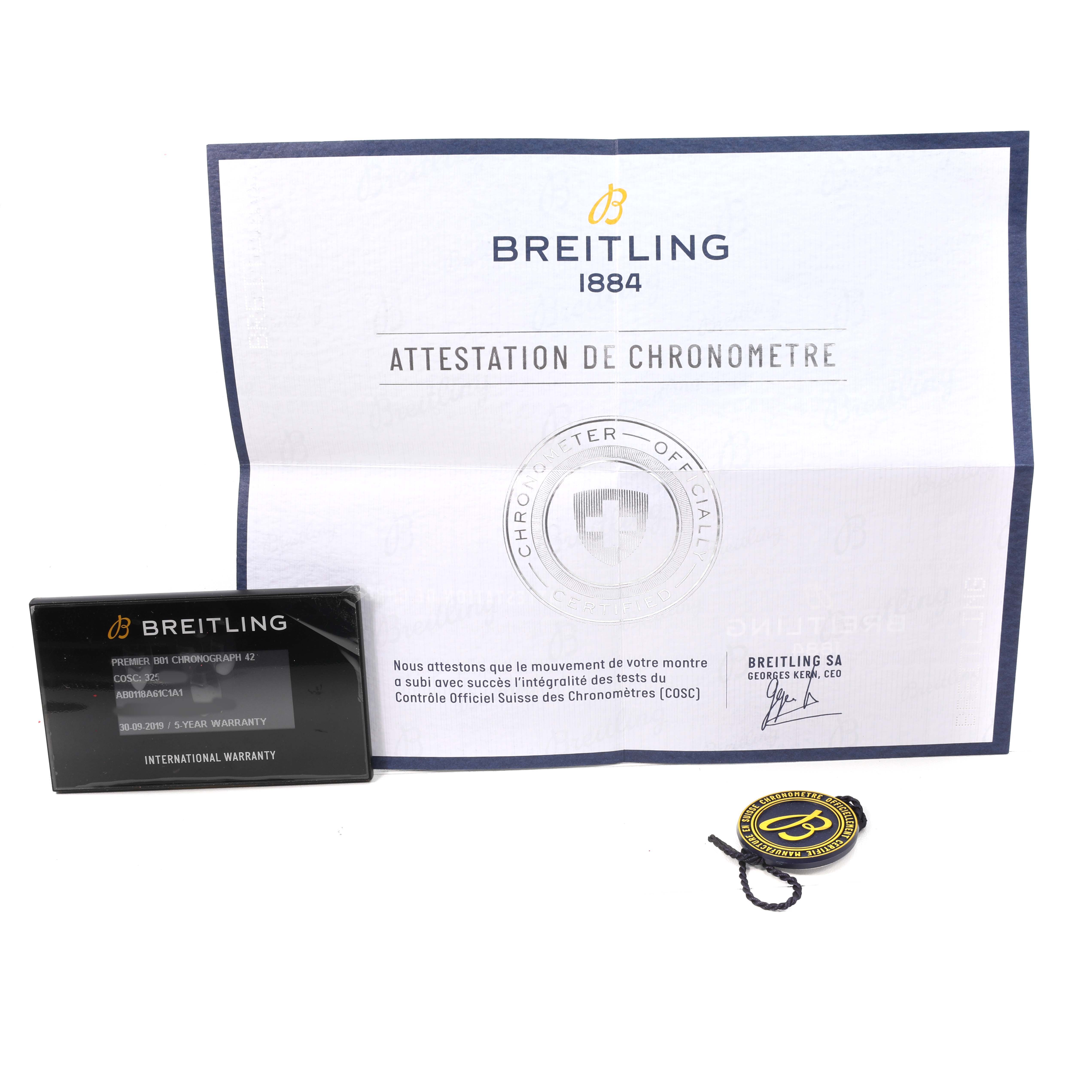 The image shows documentation and a tag for the Breitling Premier AB0118 Men's Stainless Steel Blue Dial model, including a warranty card and chronometer certificate.