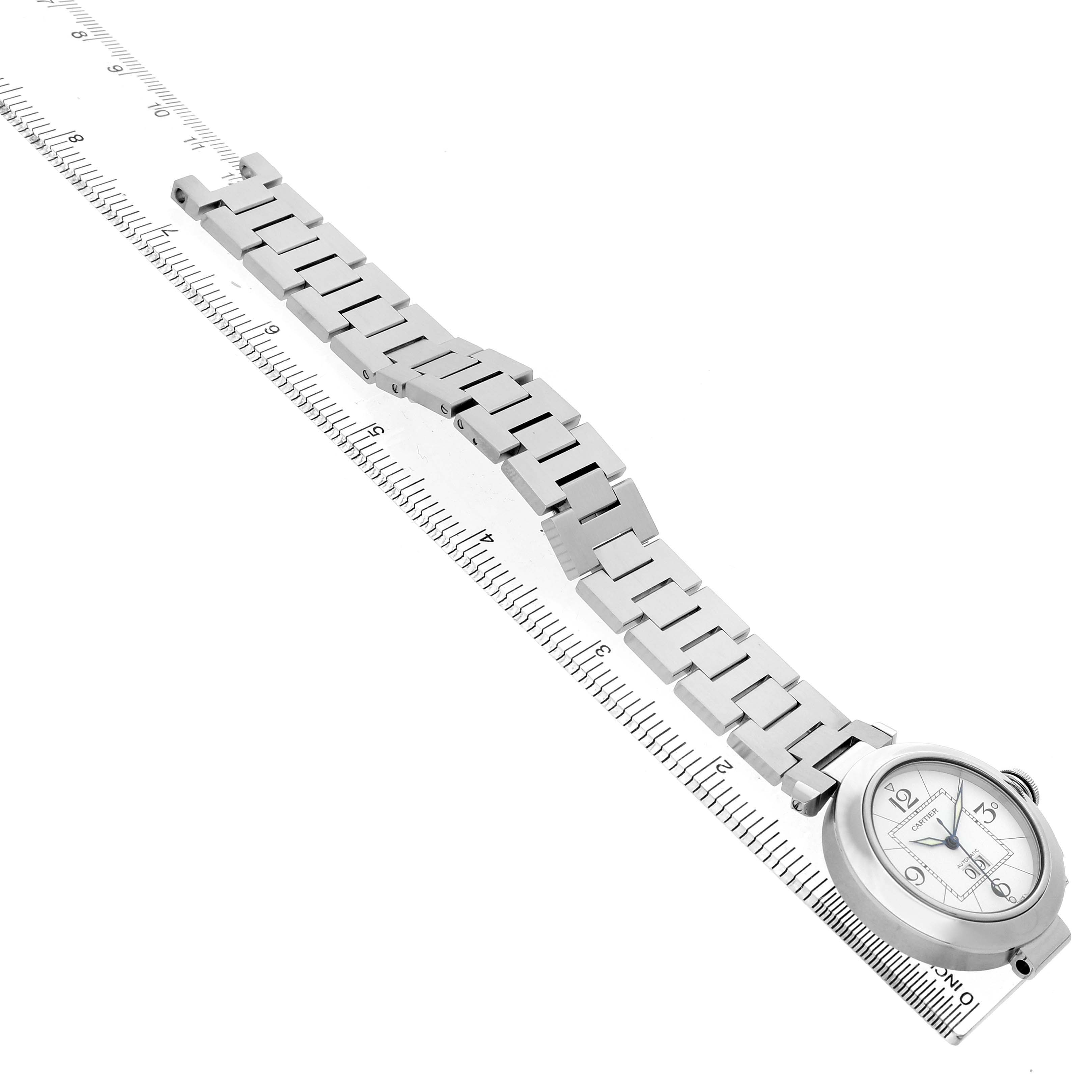 The Cartier Pasha W31055M7 Men's Stainless Steel White Dial watch is shown from a top angle, highlighting the bracelet and face aligned next to a ruler.