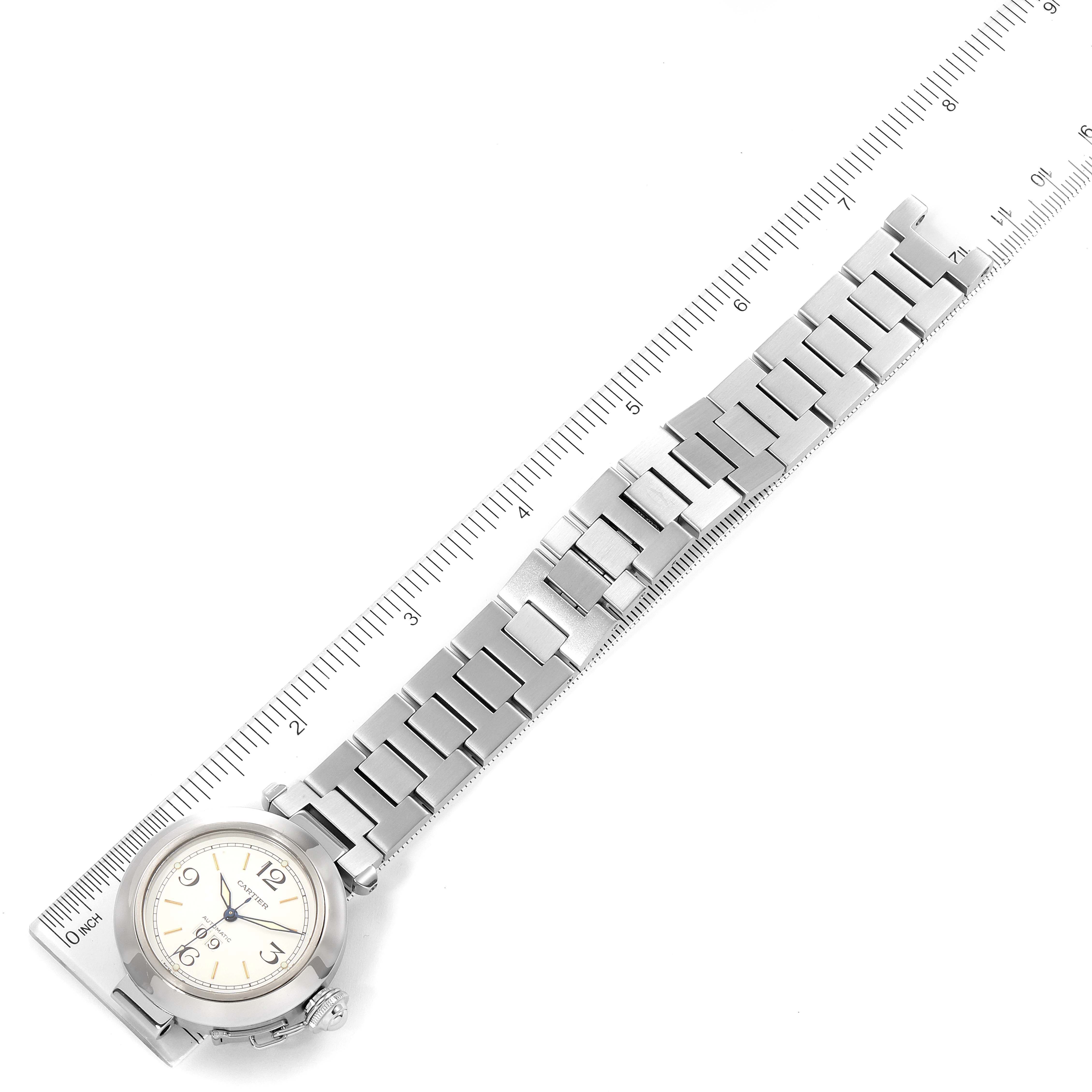 The image shows the Pasha model by Cartier placed next to a ruler, highlighting the watch face and metal bracelet from above.