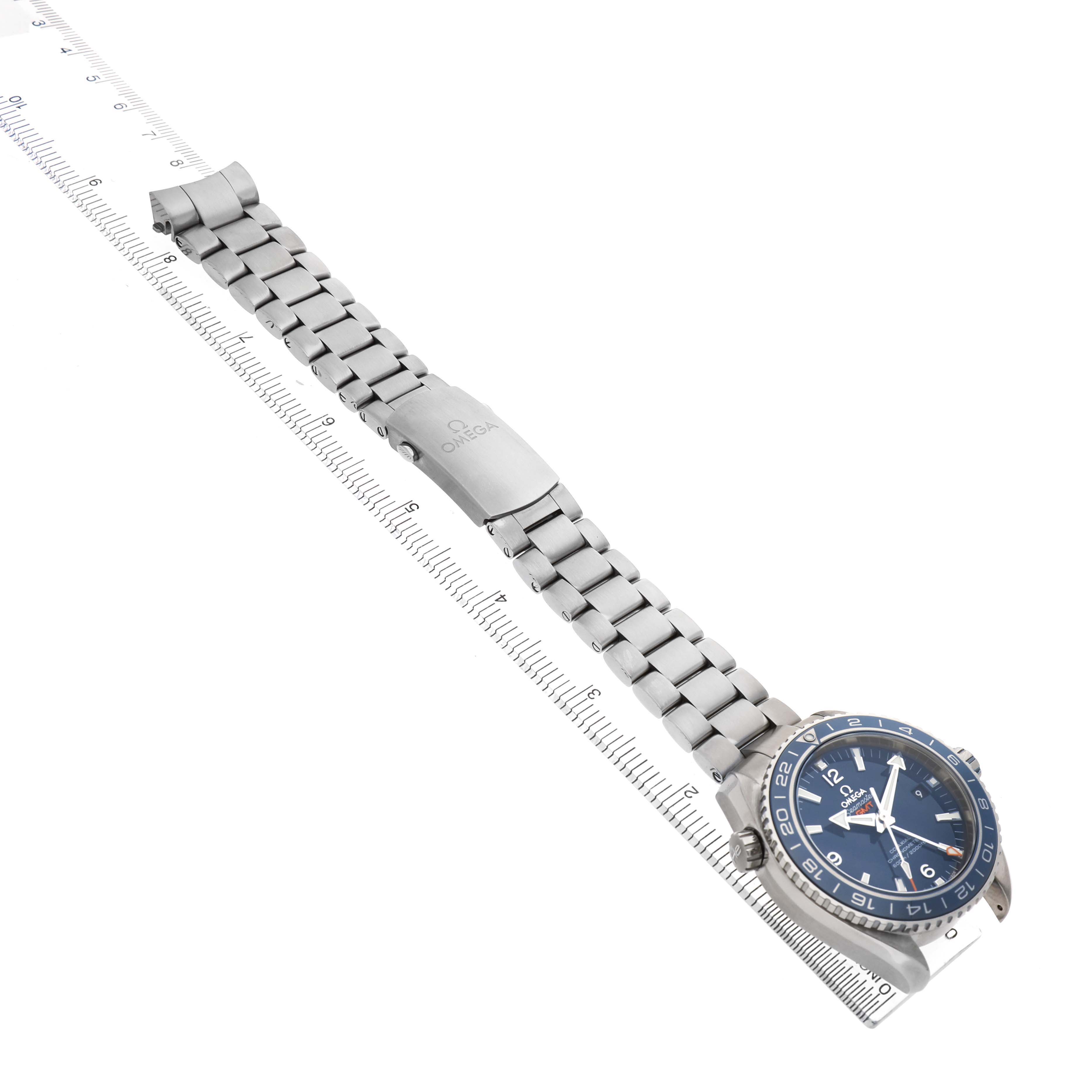 The Omega Planet Ocean 232.90.44.22.03.001 Men's Titanium Blue Dial watch is shown at an angle, highlighting its bracelet and clasp alongside a ruler for scale.
