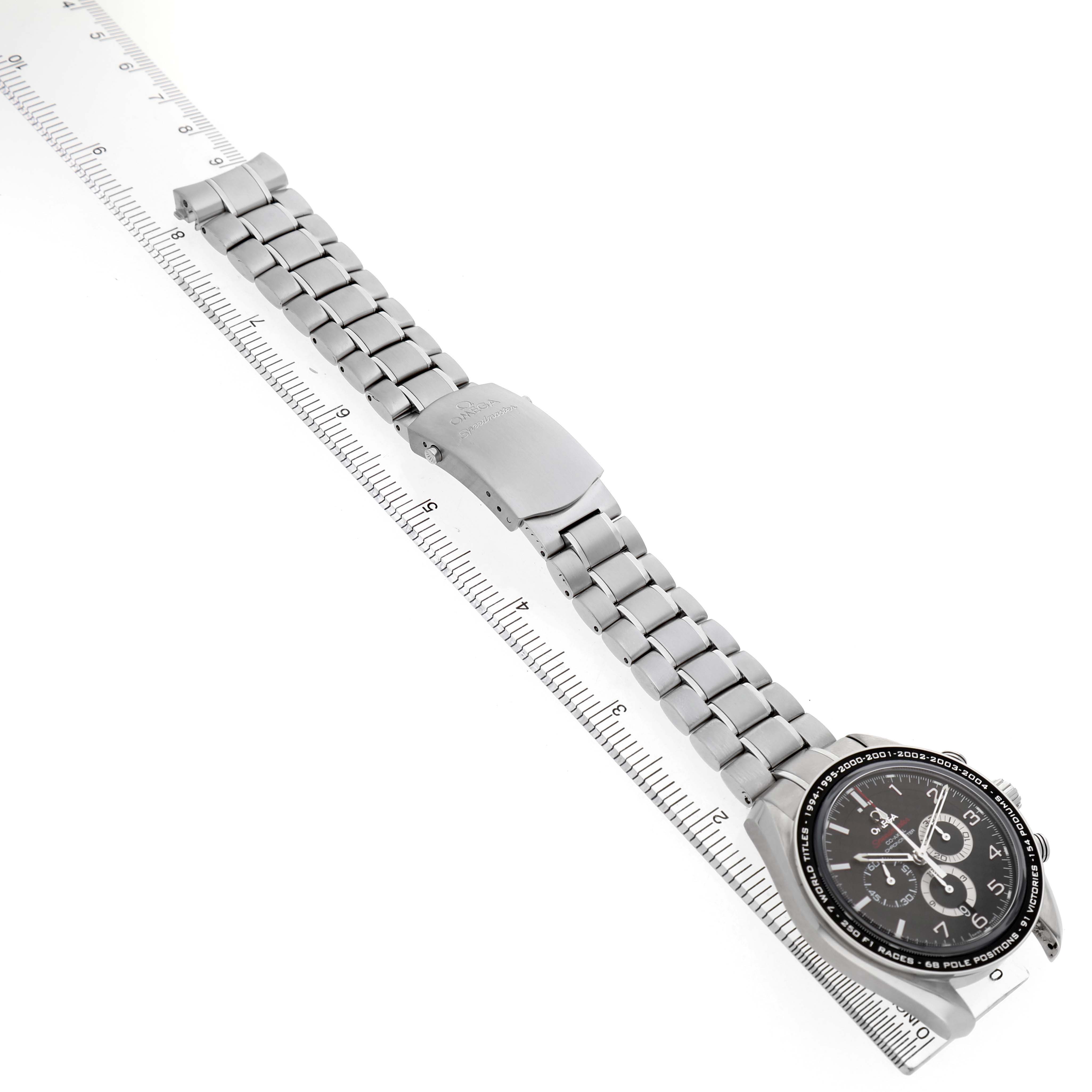 The Omega Speedmaster 321.30.44.50.01.001 Men's Stainless Steel Black Dial watch is shown diagonally from an overhead angle, with its bracelet and clasp visible alongside a ruler.