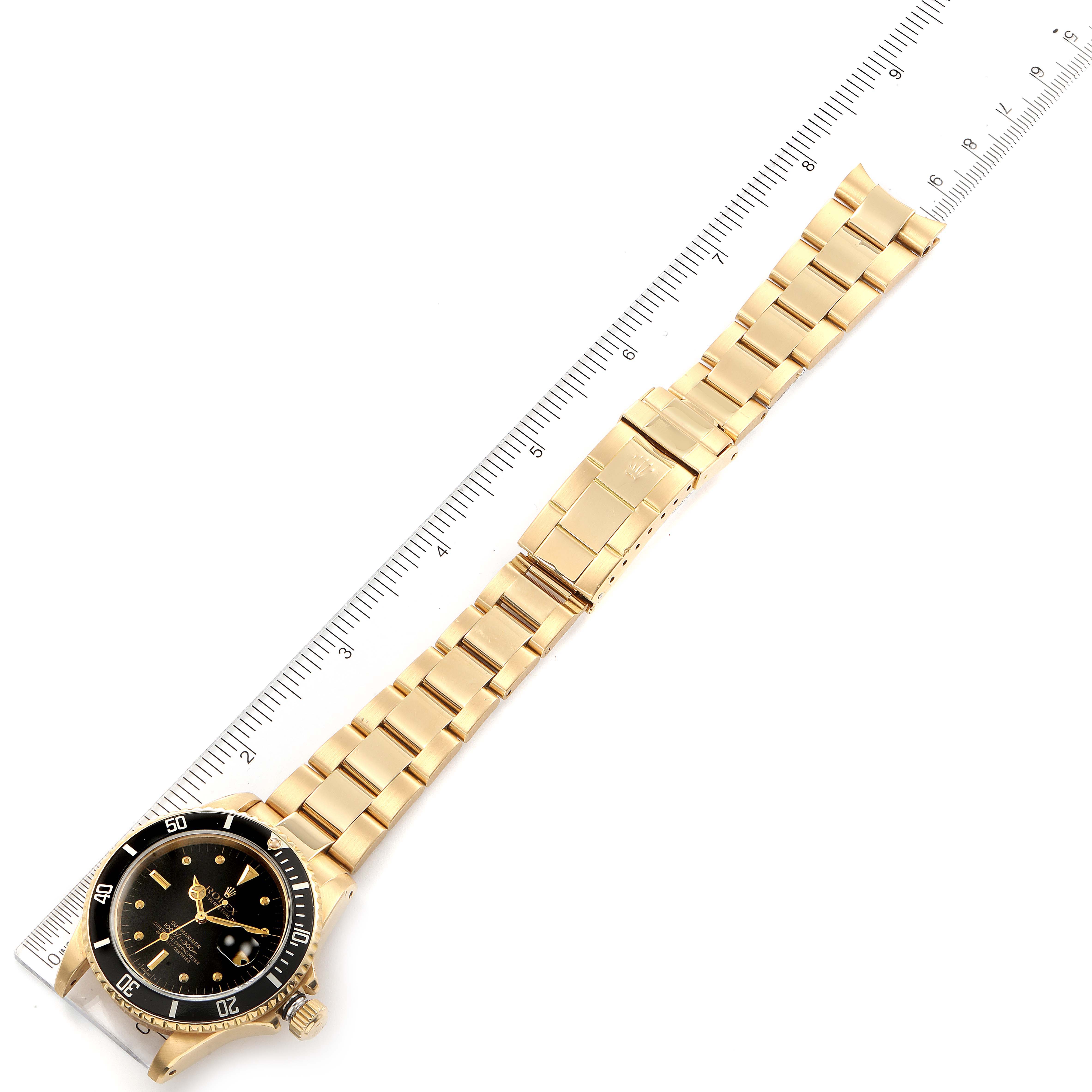 The image shows the entire Rolex Submariner 16808 Men's Yellow Gold Black Dial 16808 Men's Yellow Gold Black Dial watch at an angle with a ruler placed beside it for size reference.