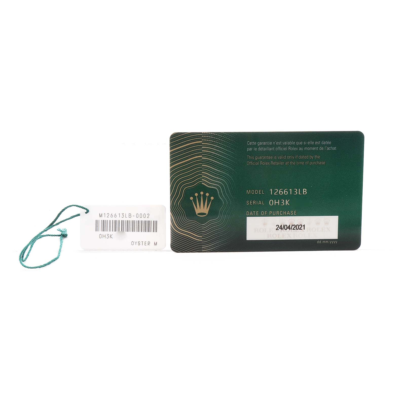 The image shows a Rolex Submariner M126613LB-0002 Men's Stainless Steel Blue Dial model card with a serial tag and a green string seal.