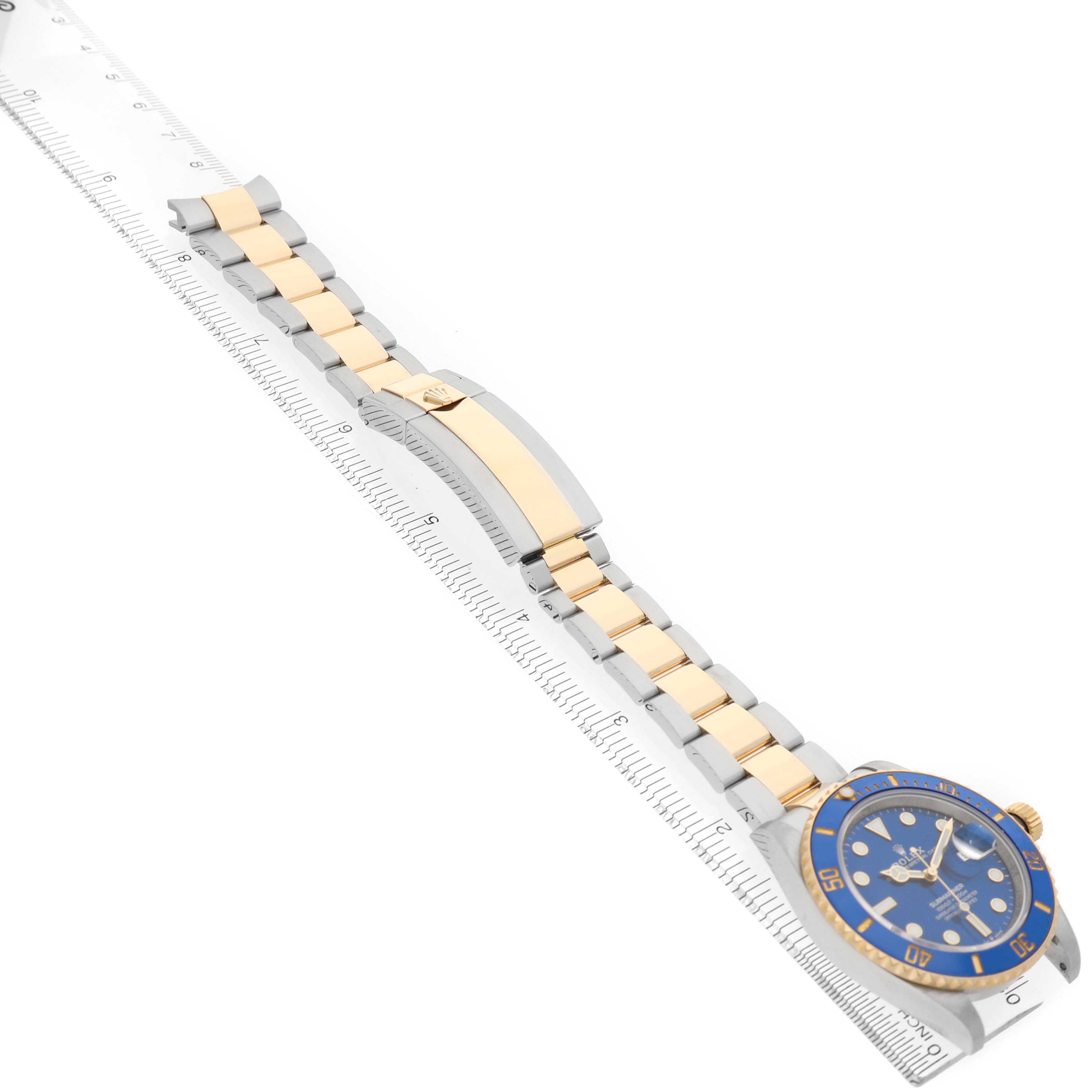 The image shows a Rolex Submariner M126613LB-0002 Men's Stainless Steel Blue Dial watch at an angle highlighting the bracelet, clasp, and face, next to a ruler for scale.
