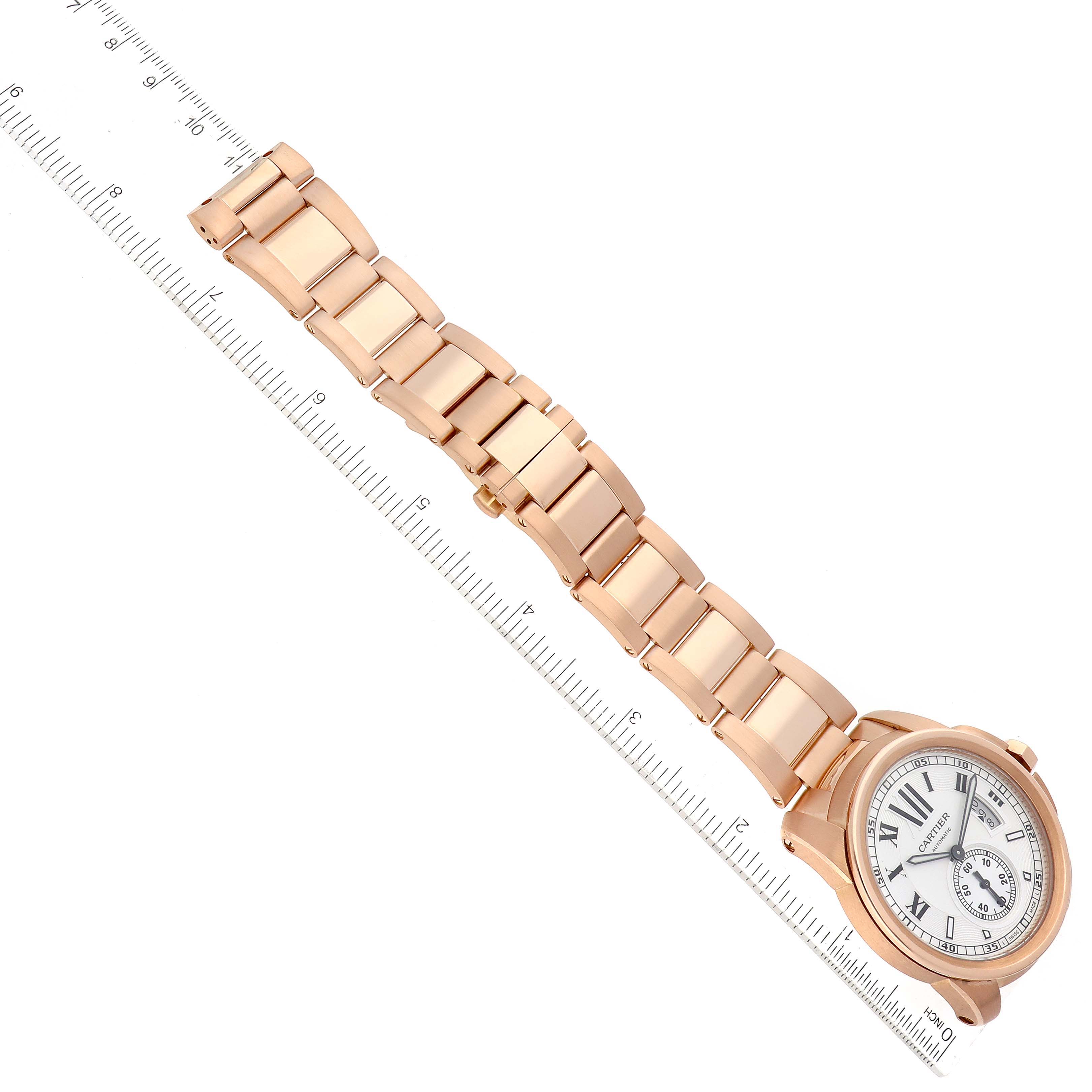 The image shows a Calibre de Cartier watch by Cartier from a top-down angle, highlighting its bracelet and dial with a ruler for scale.