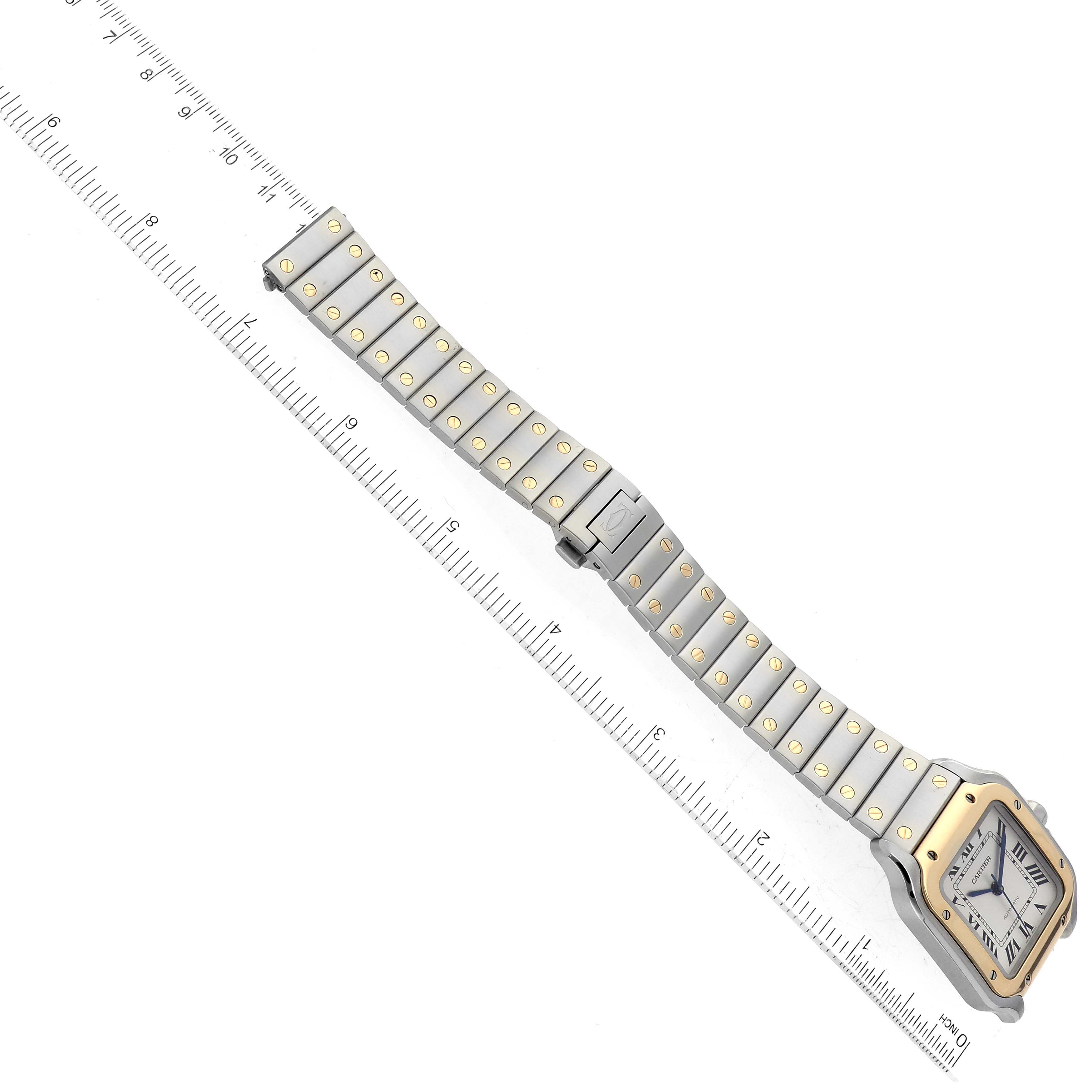 This Cartier Santos W2SA0007 Men's Steel and Gold (two tone) Silver Dial W2SA0007 Men's Steel and Gold (two tone) Silver Dial watch is shown from a top-down angle, displaying the face and full bracelet stretched alongside a ruler.