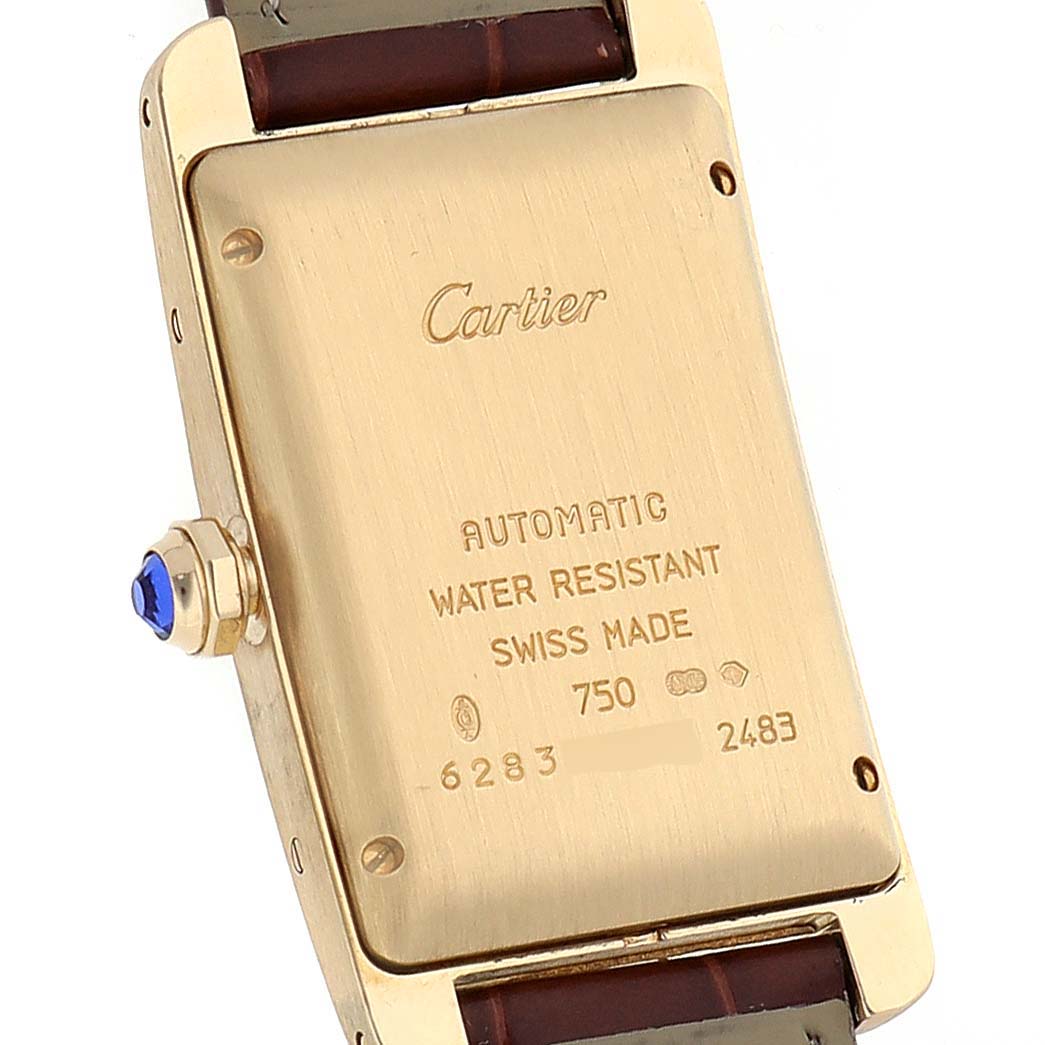 The image shows the back case of a Cartier Tank Americaine W2603556 Men's Yellow Gold Silver Dial W2603556 Men's Yellow Gold Silver Dial watch, highlighting engravings and the crown with a blue jewel.