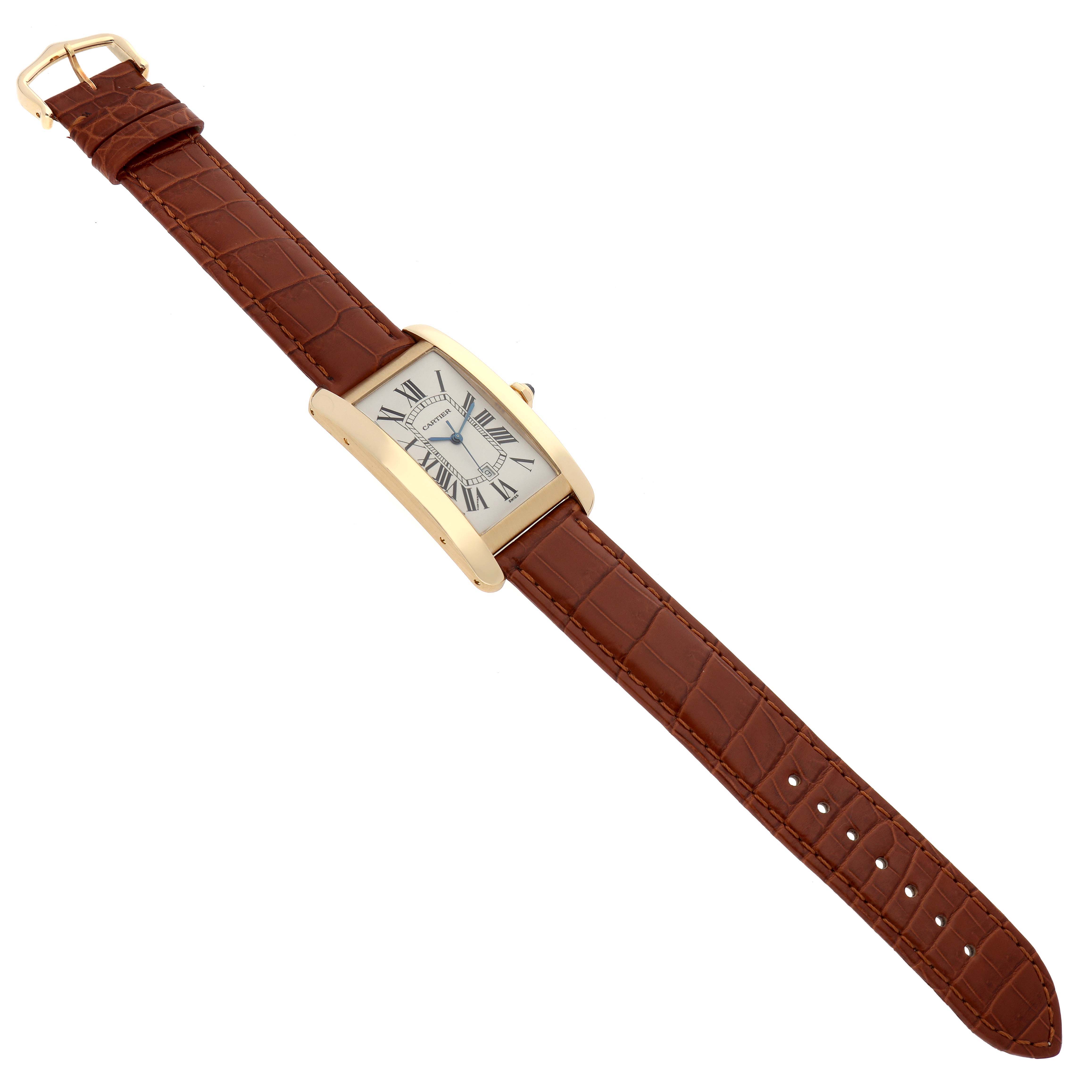 The image shows a Cartier Tank Americaine W2603156 Men's Yellow Gold Silver Dial W2603156 Men's Yellow Gold Silver Dial watch in a top-down angle, displaying its rectangular dial, leather strap, and buckle.