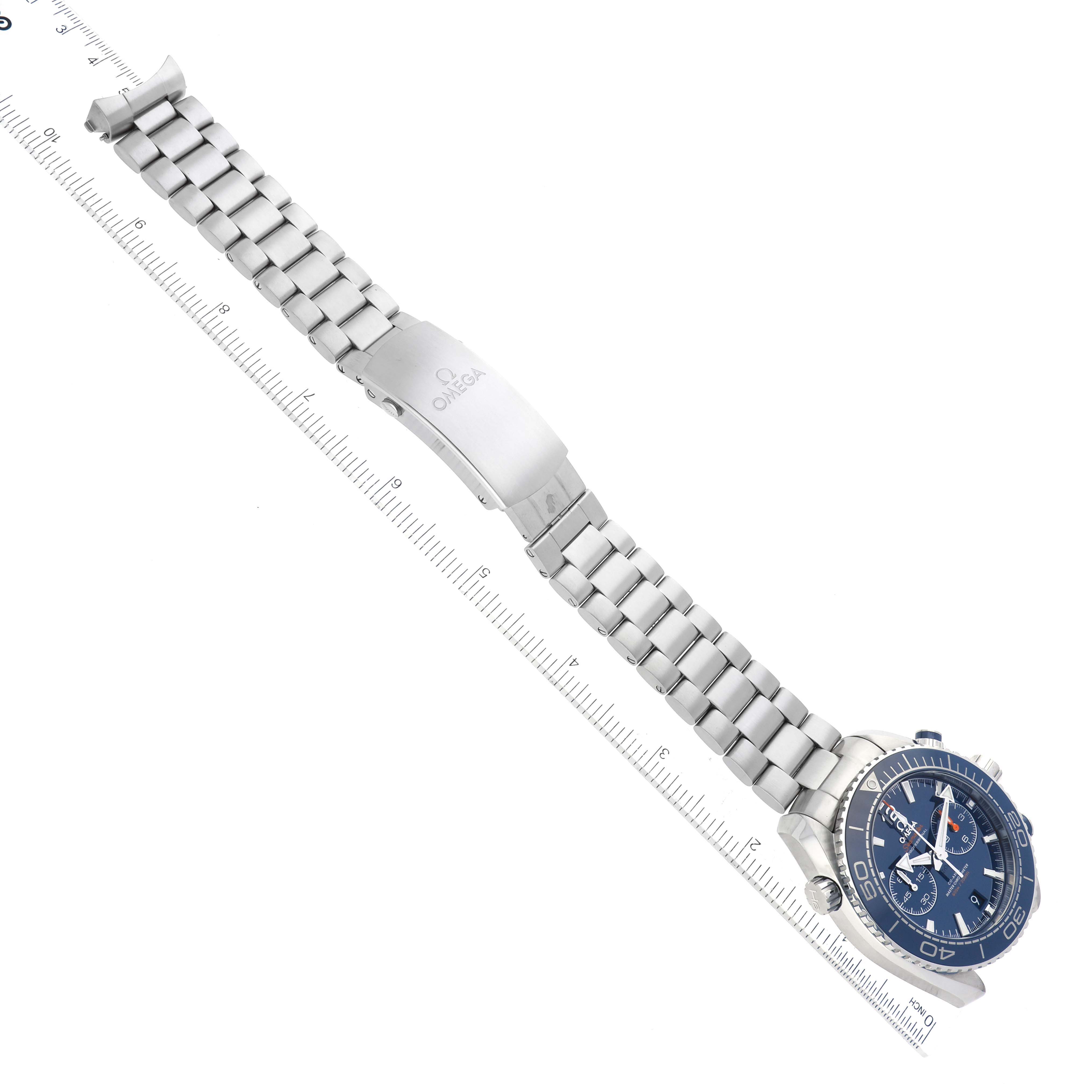 The image shows an Omega Planet Ocean 215.30.46.51.03.001 Men
s Stainless Steel Blue Dial 215.30.46.51.03.001 Men
s Stainless Steel Blue Dial watch lying flat with its metal bracelet extended beside a ruler for scale.