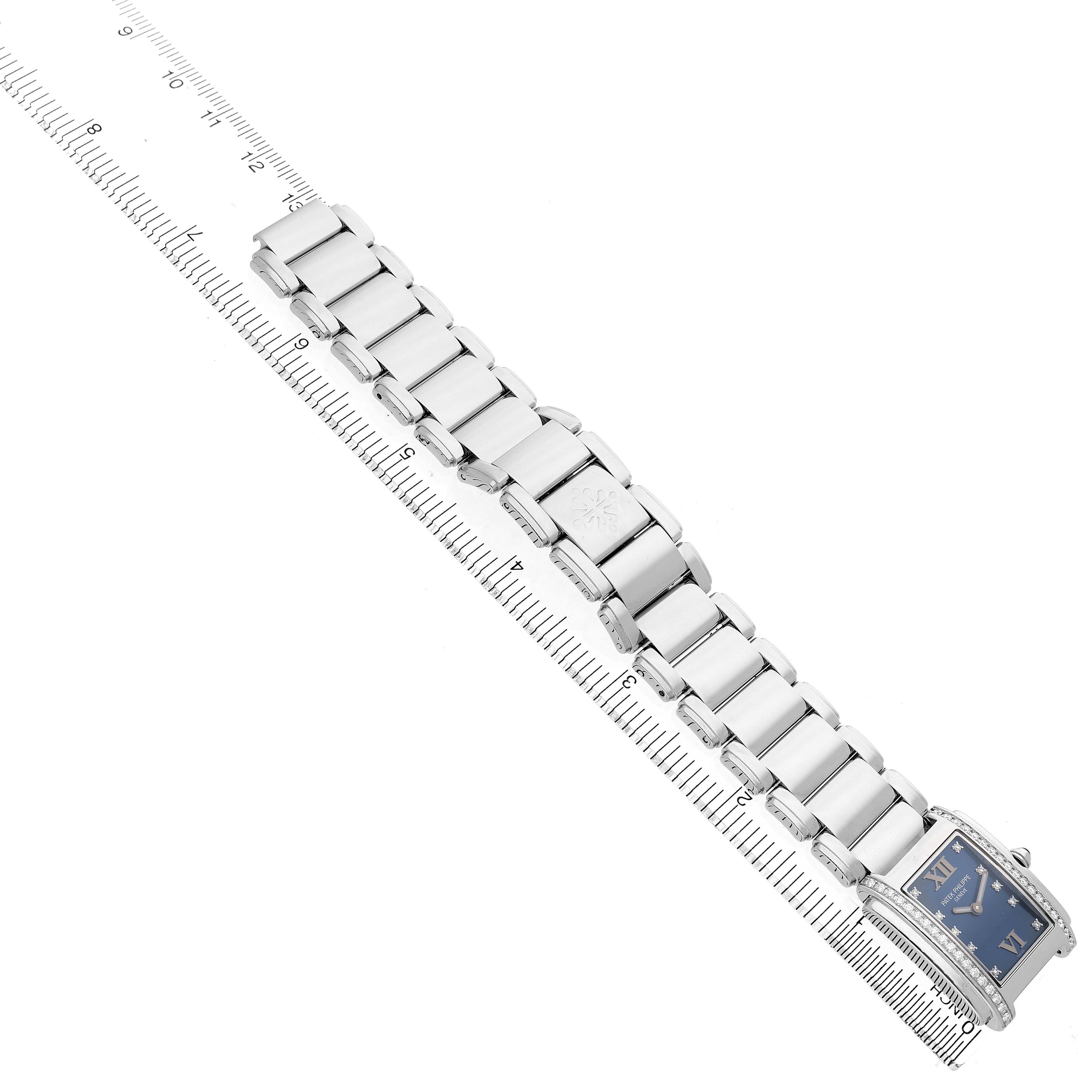 The Patek Philippe Twenty-4 4910 4910A Women's Stainless Steel Blue Dial watch is shown at an angled top view with a blue dial, and its bracelet is laid out along a ruler.