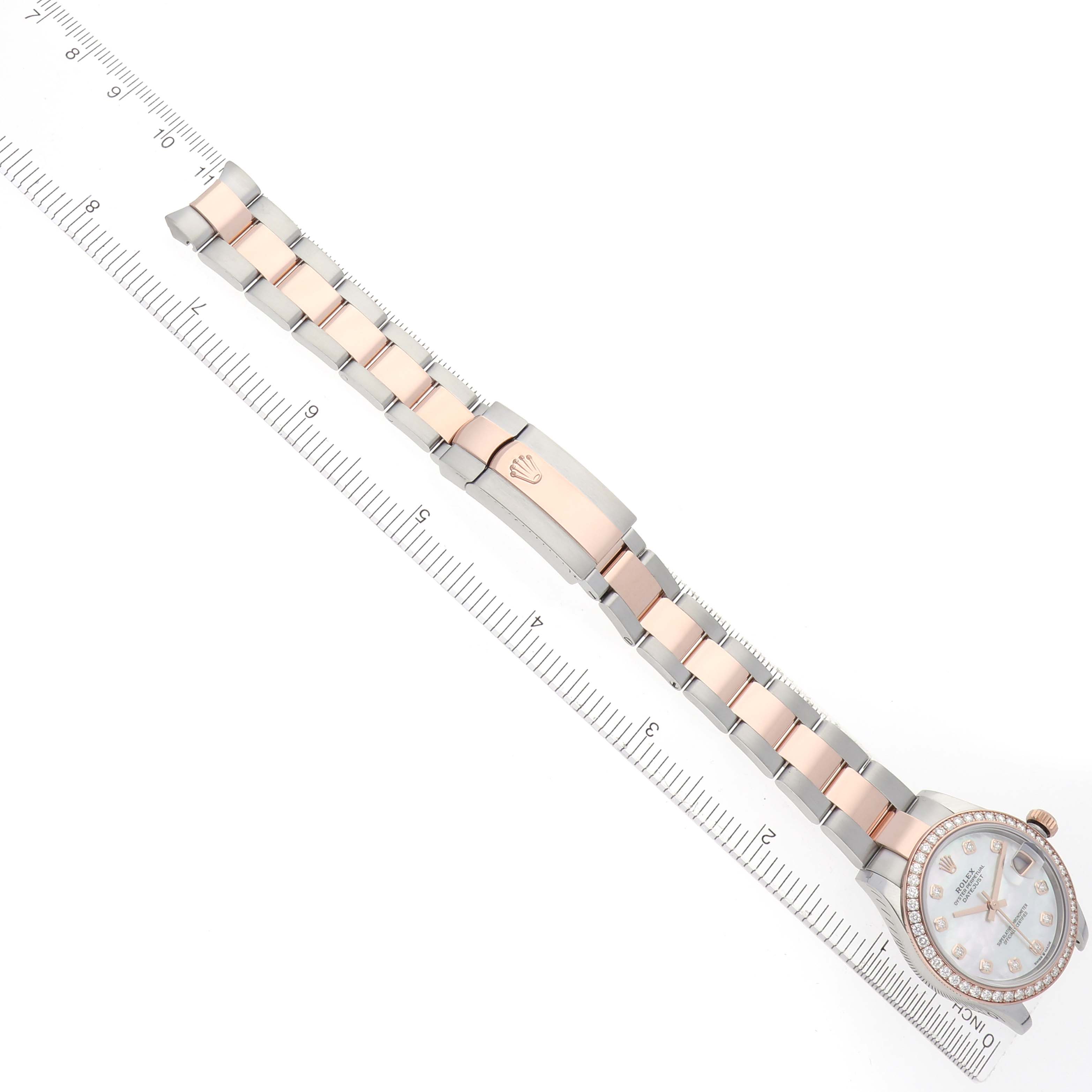 The Rolex Datejust watch is shown at an angle, displaying the face, bracelet, clasp, and part of a ruler for scale.