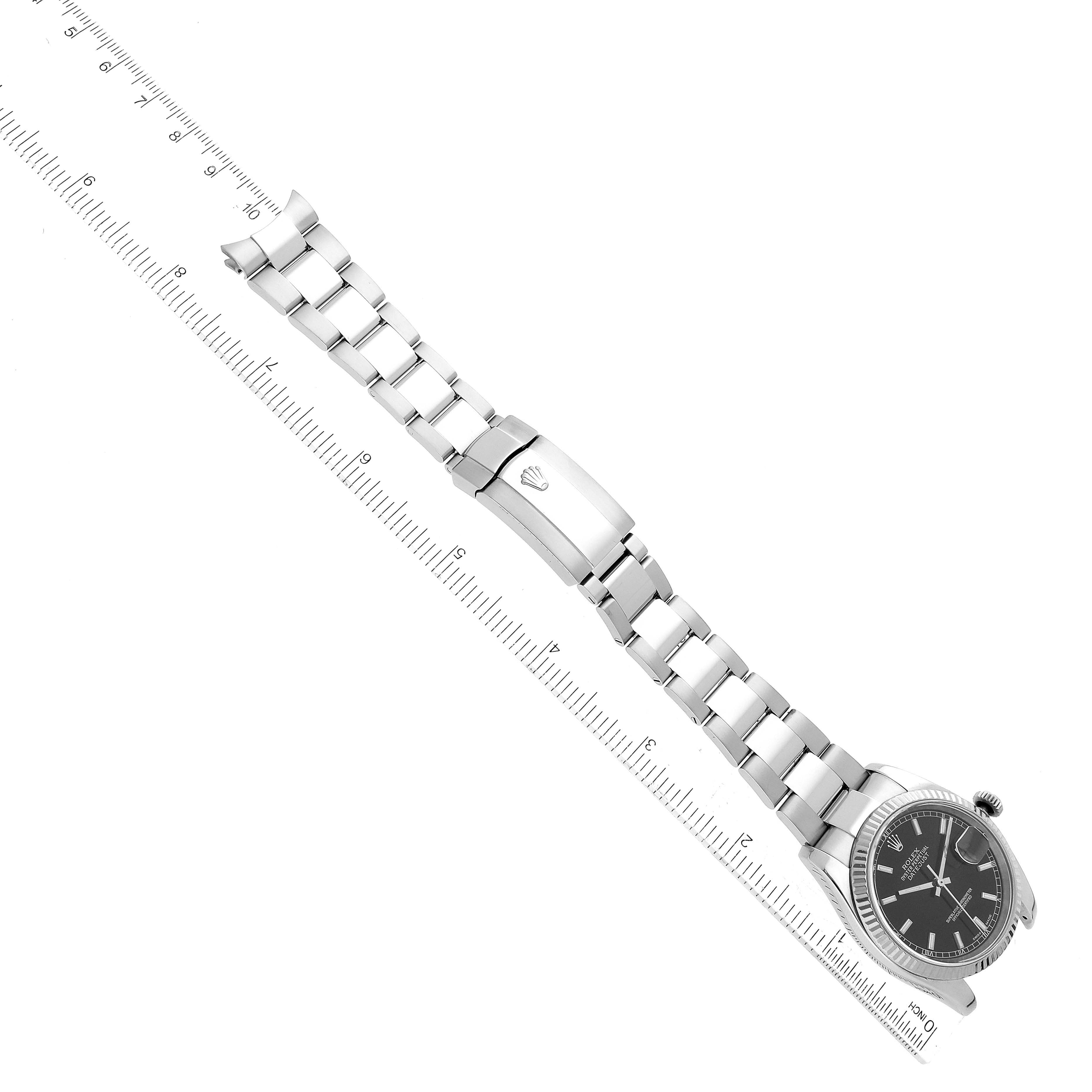 The image shows a Rolex Datejust 116234 Men's Stainless Steel Black Dial 116234 Men's Stainless Steel Black Dial watch at a diagonal angle, displaying its bracelet and clasp, alongside a ruler for scale.